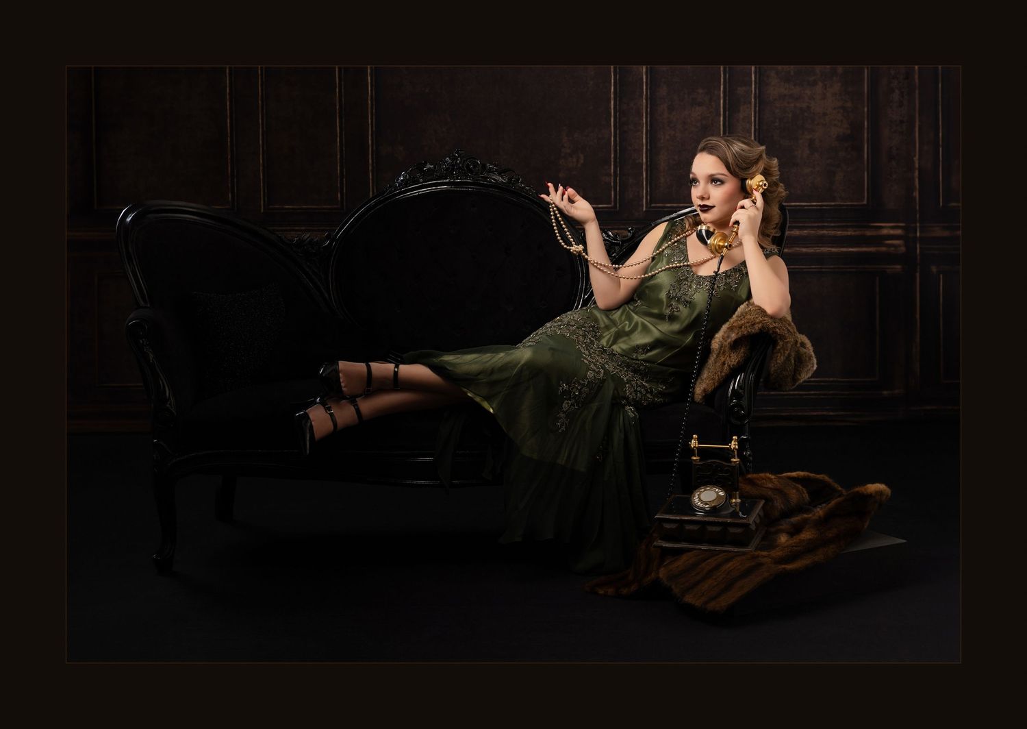Woman in green dress reclines on vintage sofa talking on antique telephone in dark elegant room.