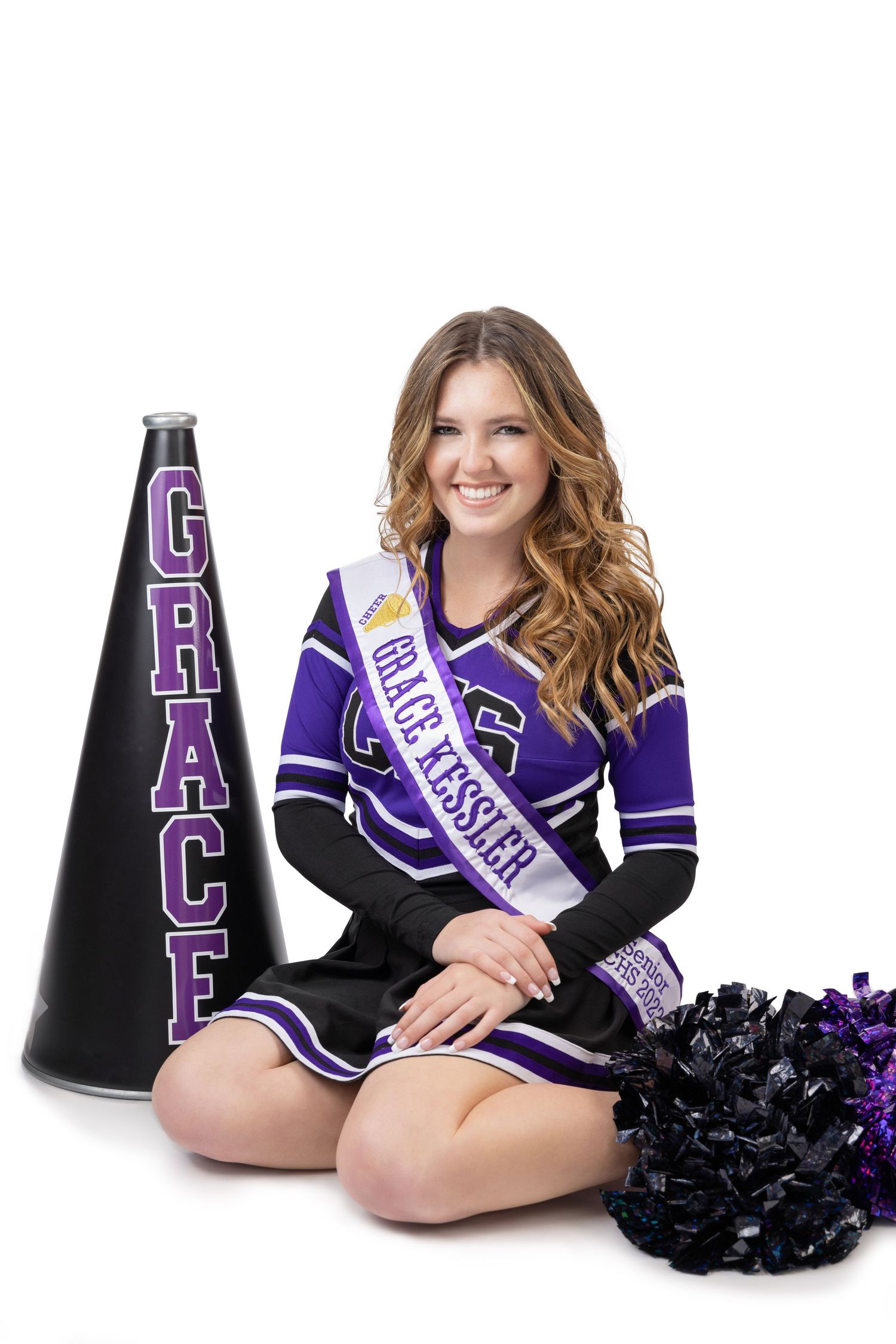 Cheerleader Grace Kessler in purple uniform sitting with megaphone and pom-poms on white background.