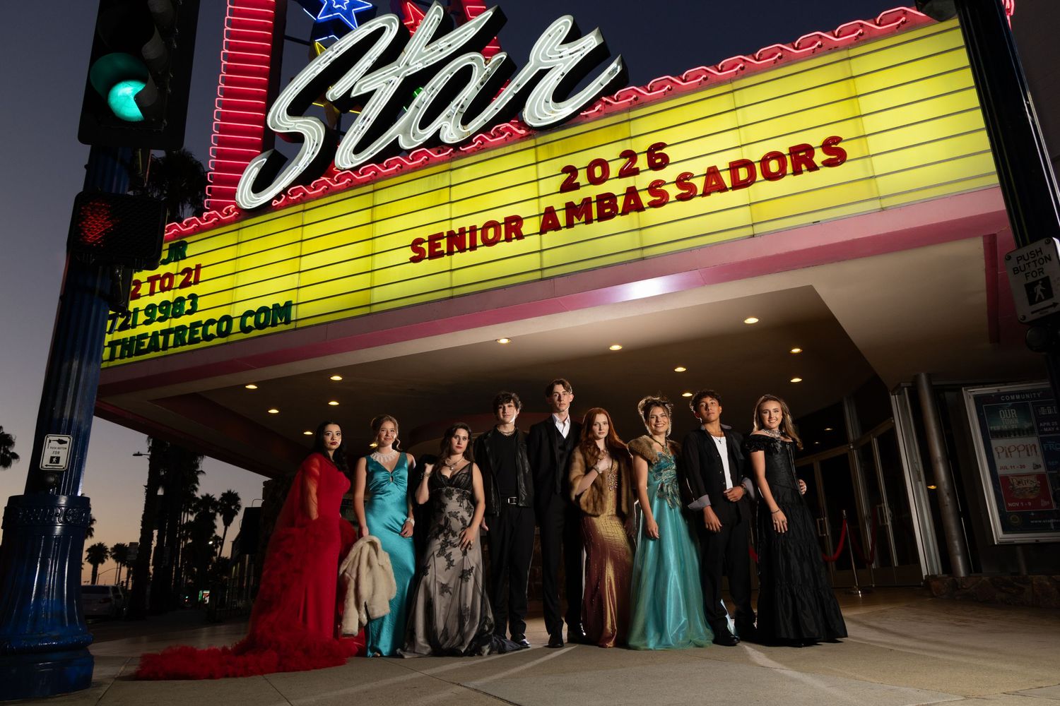 Group of 2025 Senior Ambassadors posing in formal attire under a Star Theatre marquee at night.