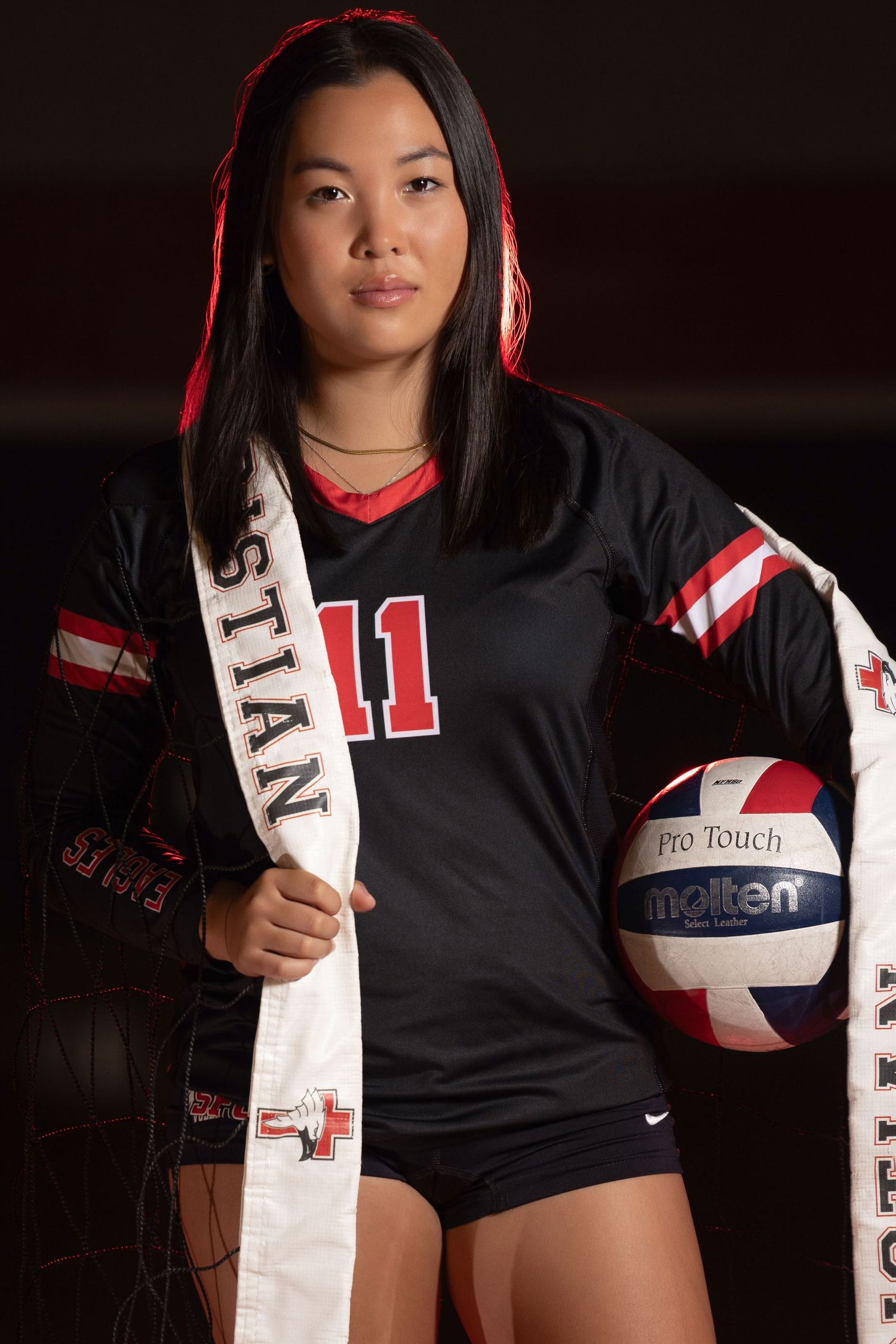 Female volleyball player number 11 in black uniform holding a Molten ball with a sash in a dramatic portrait.