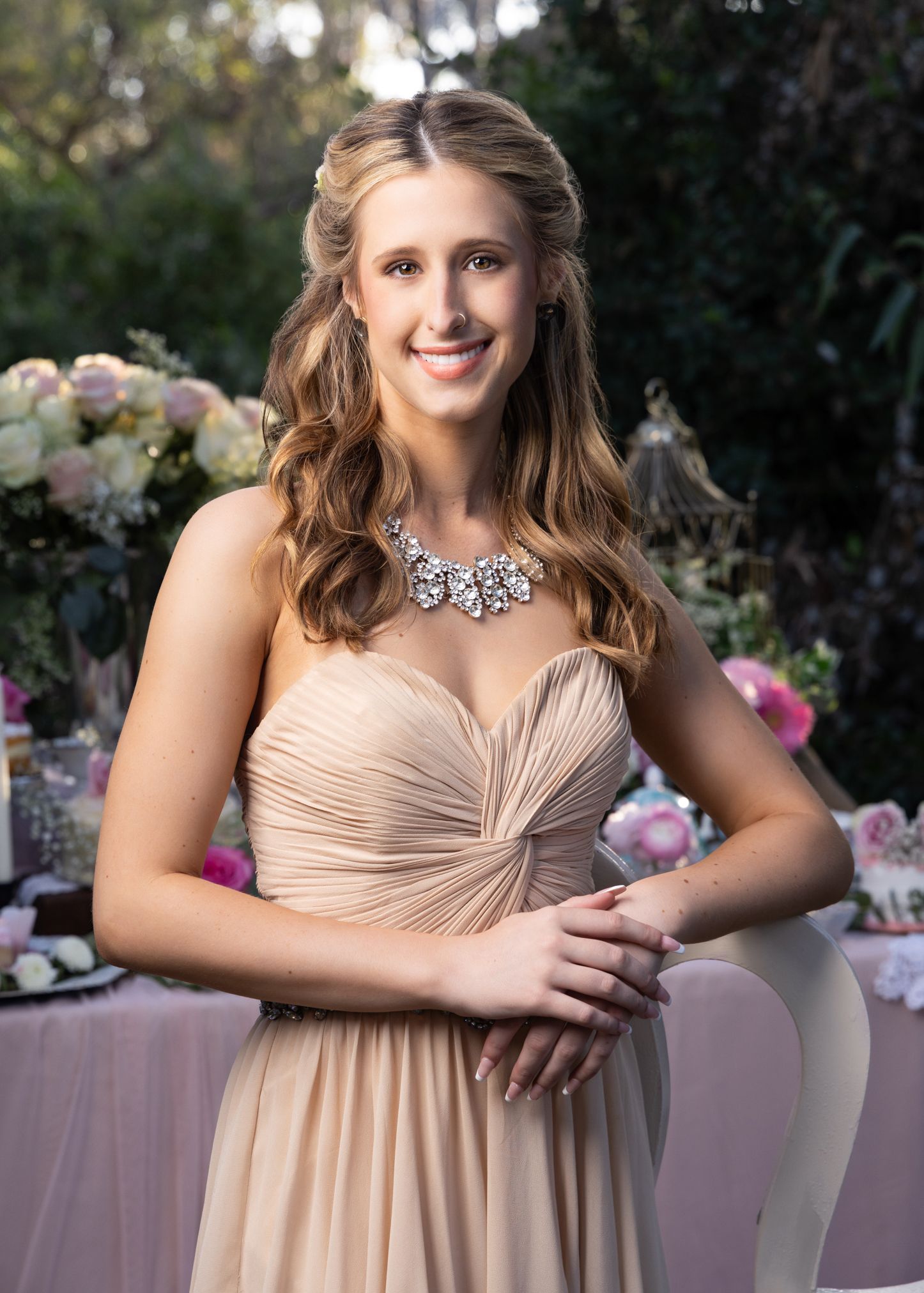 Smiling woman in champagne strapless gown with crystal necklace at romantic garden party.