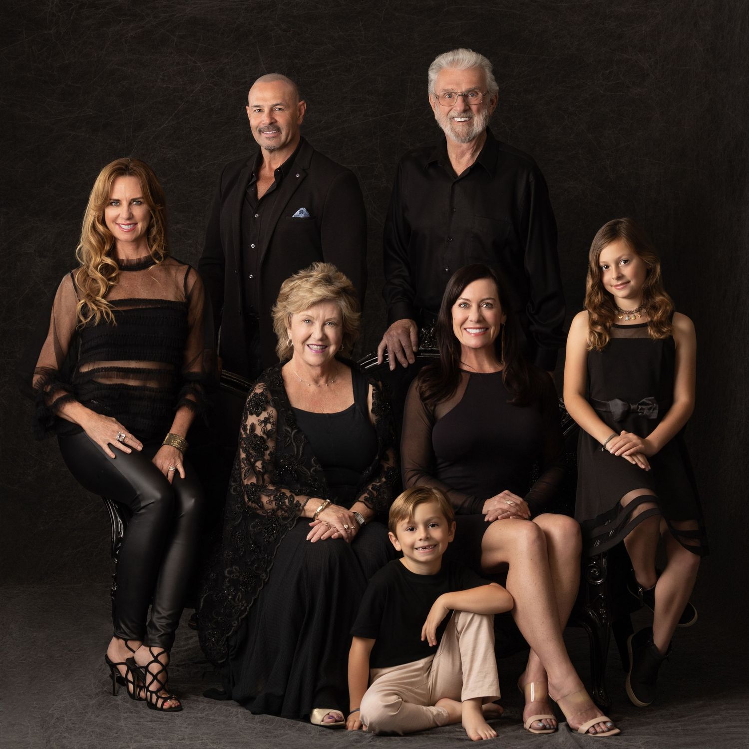 Family portrait of seven people dressed in elegant black outfits posing together in a professional studio setting.