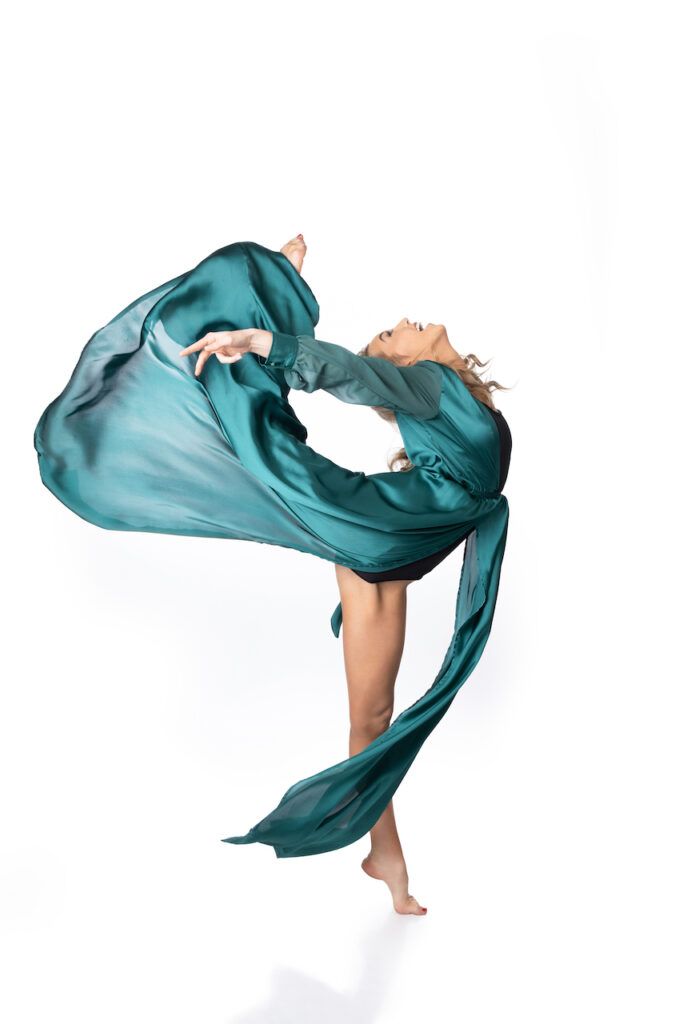 Graceful dancer performing a backbend in flowing teal fabric against a clean white studio background.