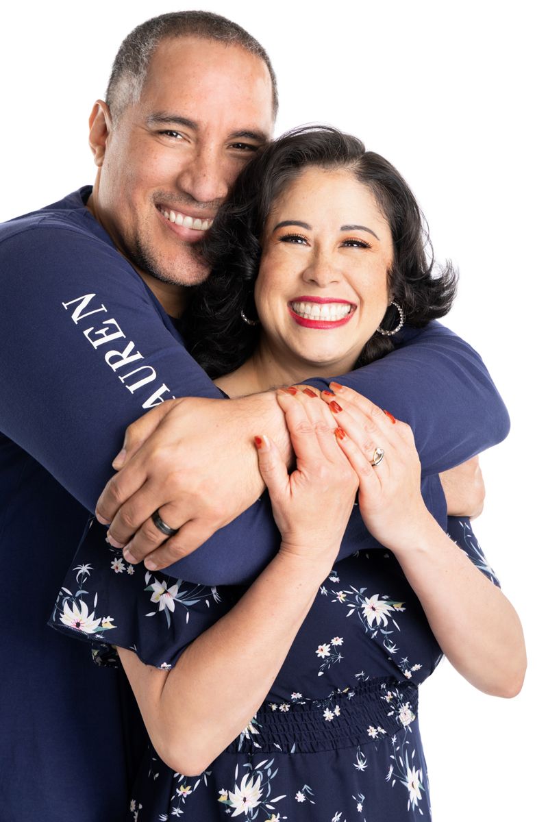 Happy couple embracing and smiling, woman in floral dress, man in navy Lauren shirt, white background.