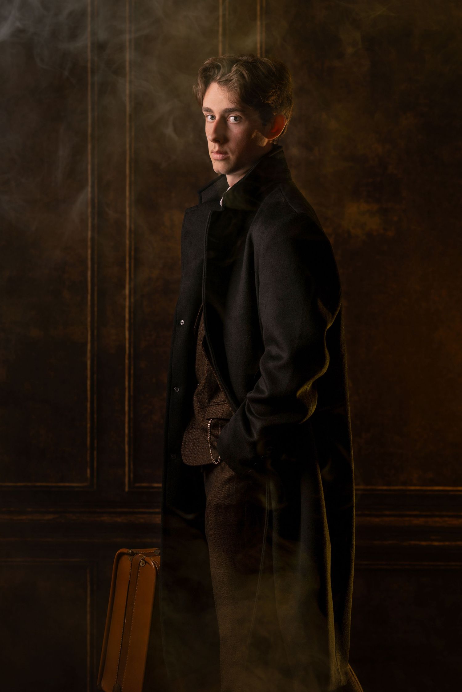 Victorian man in black trench coat holding a briefcase, posing dramatically against a dark textured wall.