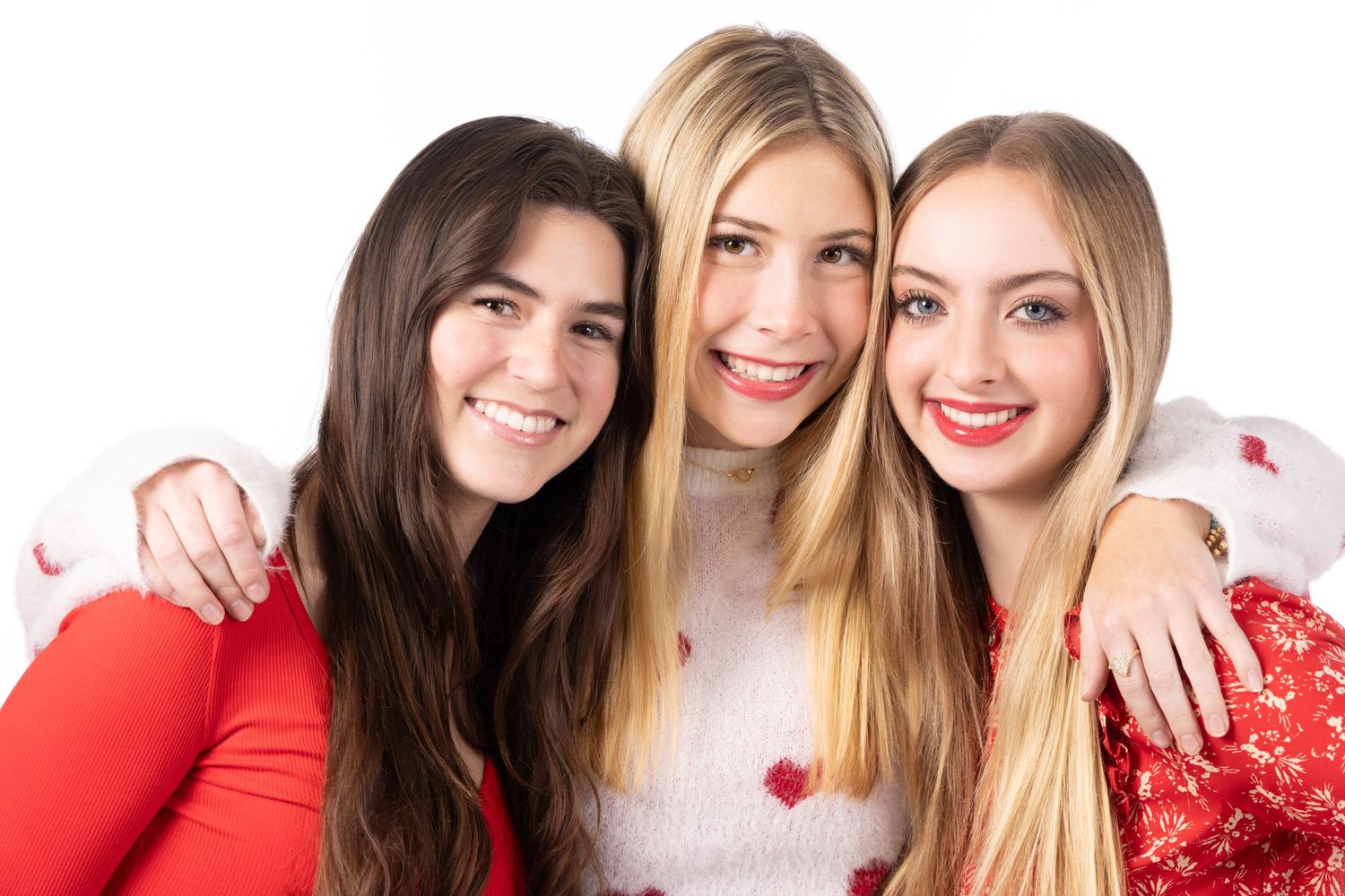 Three smiling young women posing together, two brunettes and one blonde, wearing festive red and white holiday outfits.