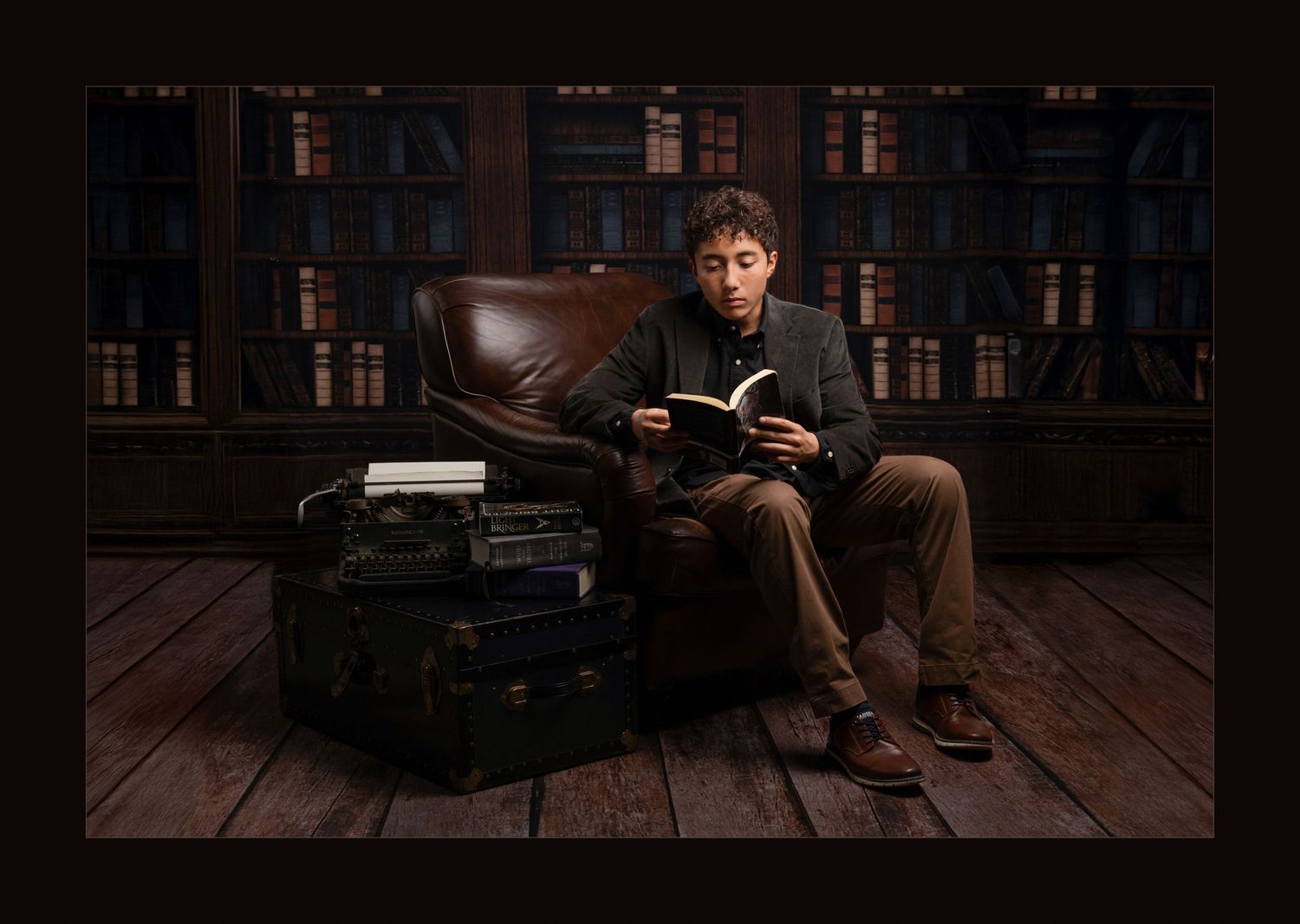 Man reads book in leather chair surrounded by shelves of books in cozy library.