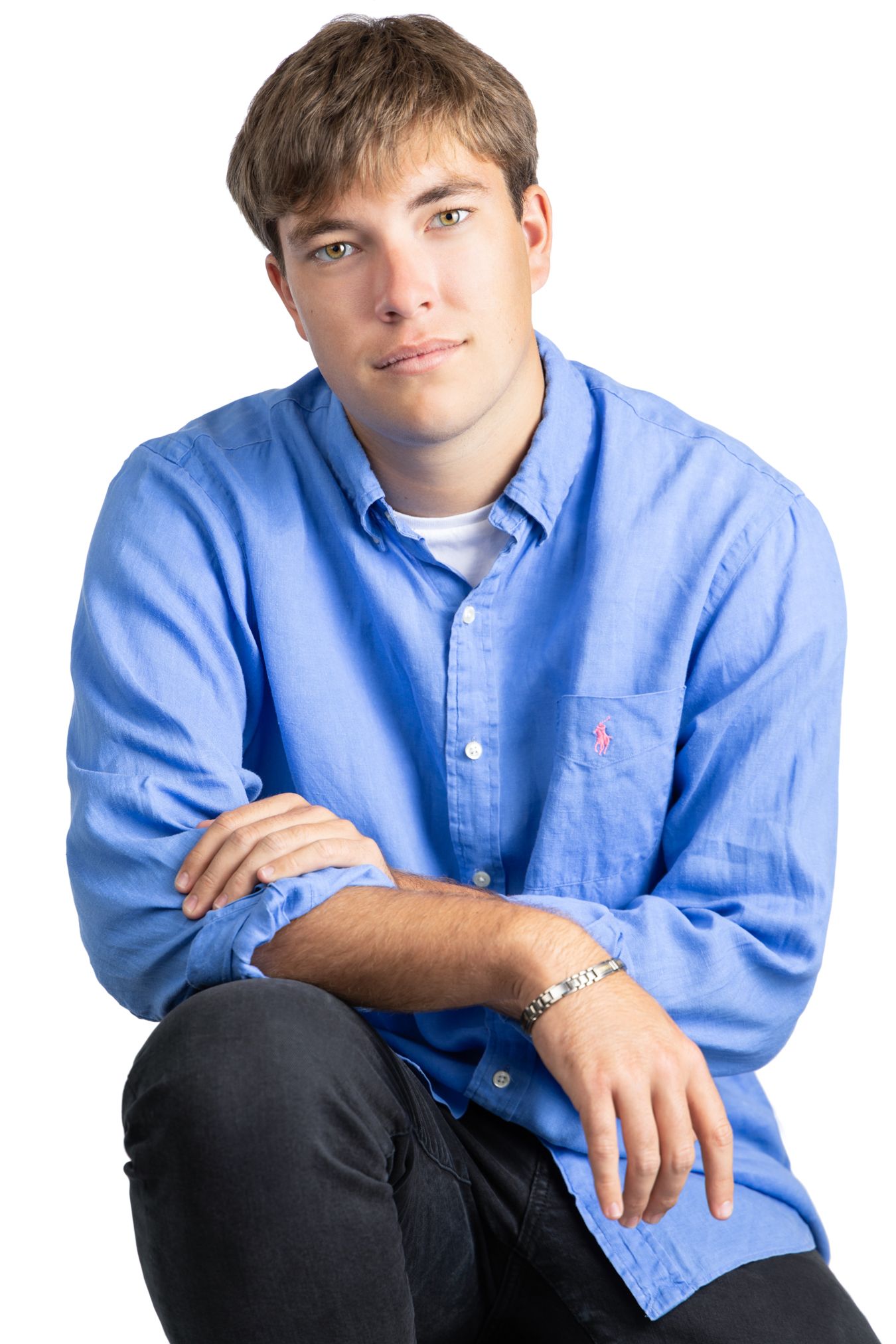 Young man in blue button-down shirt sitting casually against white background.