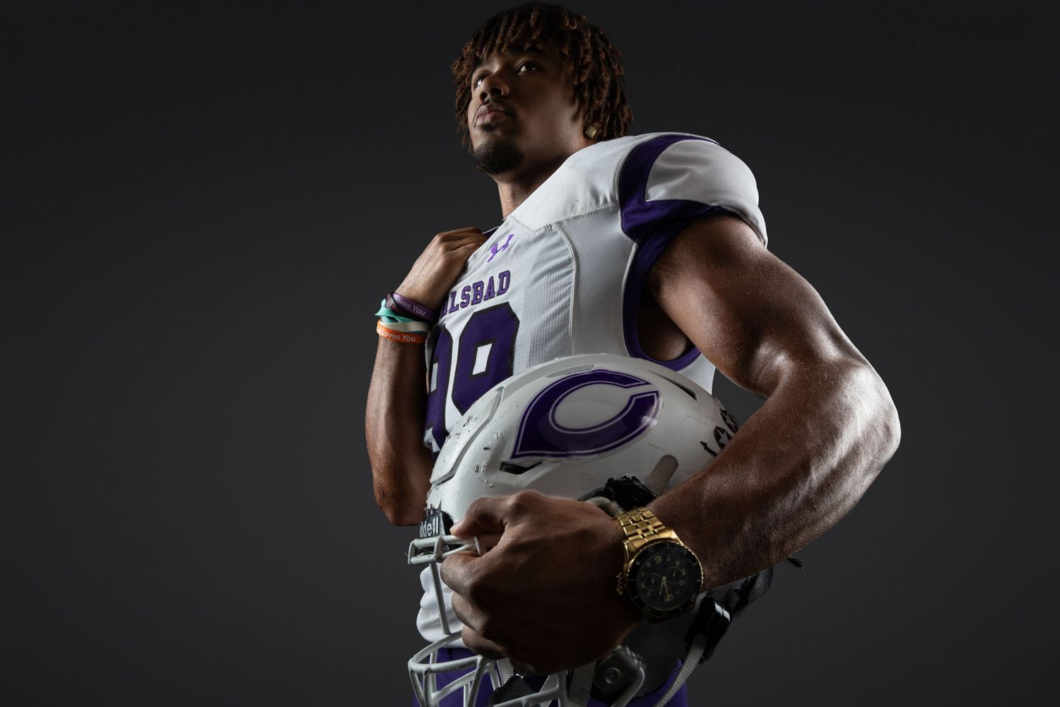A muscular football player in a purple uniform holds a helmet in a dramatic studio portrait.