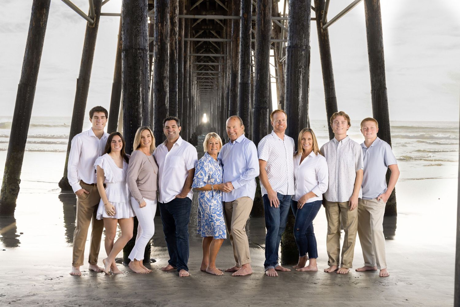 Large family group portrait posing together under a pier at the beach.