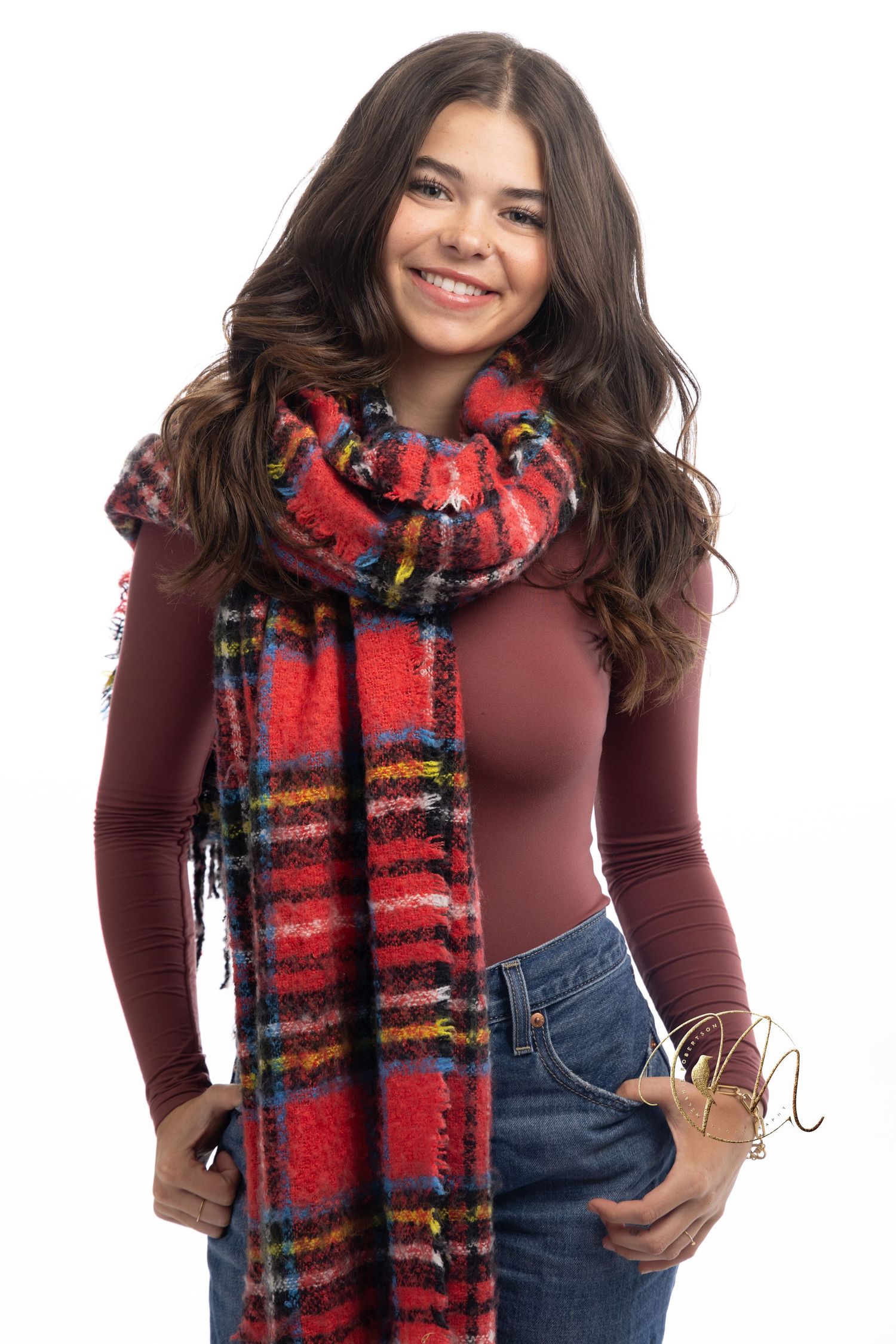 Smiling young woman wearing a red plaid scarf and burgundy top with jeans against a white background.