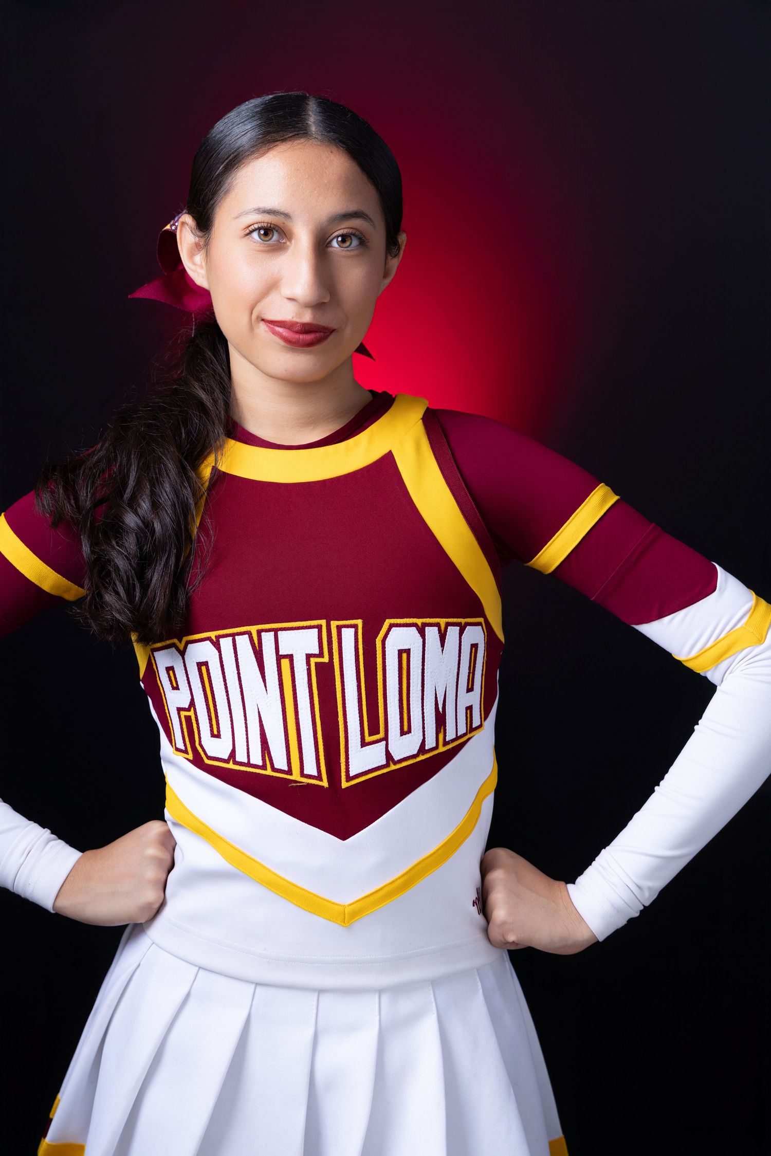 Female cheerleader in Point Loma maroon and white uniform posing against a red and black background.