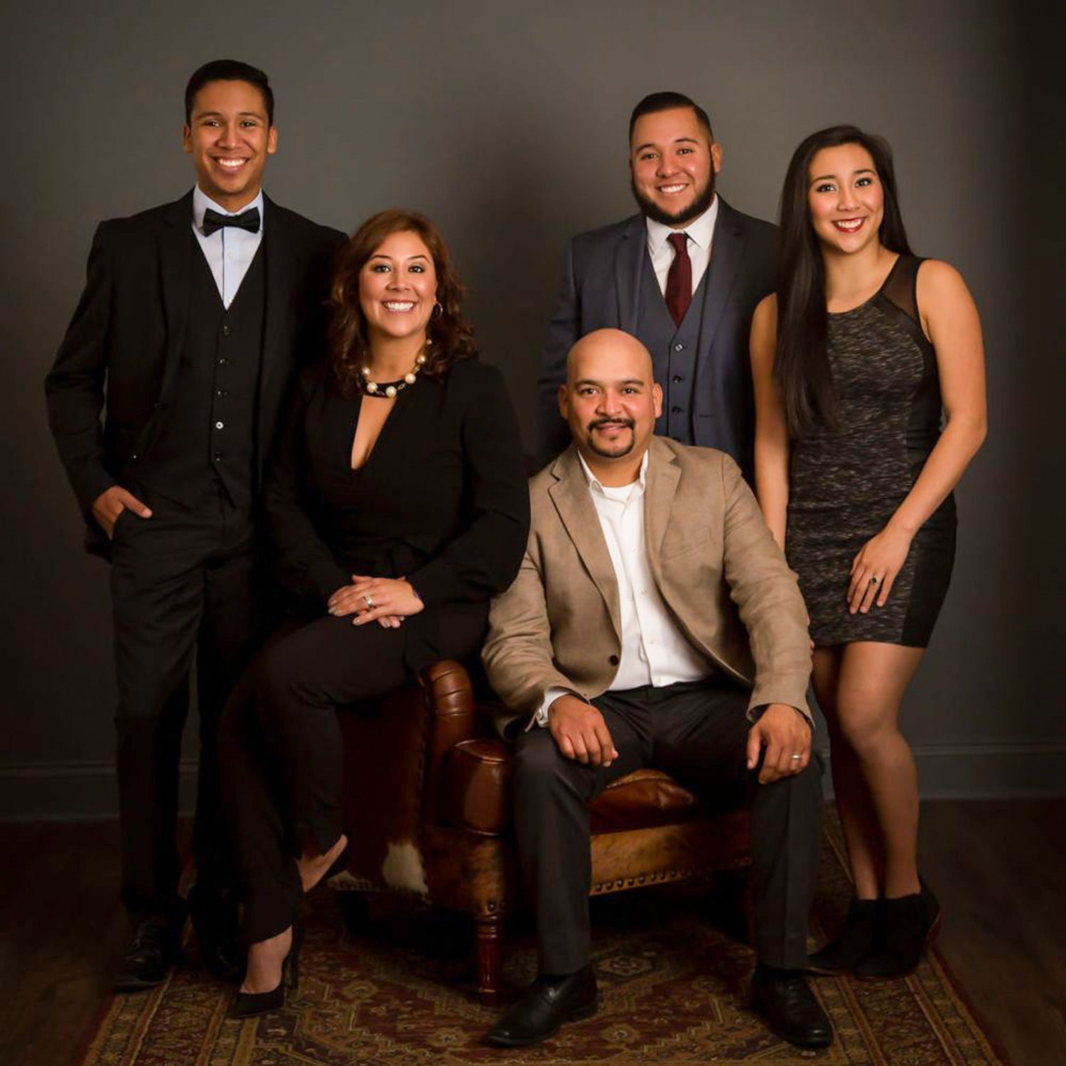 Formal family portrait of five people in elegant attire, posing together in a professional studio setting.