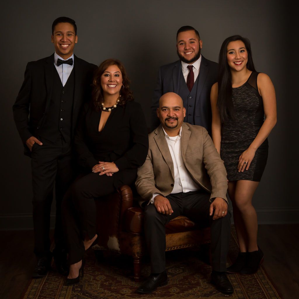 Family of five in formal wear posing together for elegant studio portrait against dark background.
