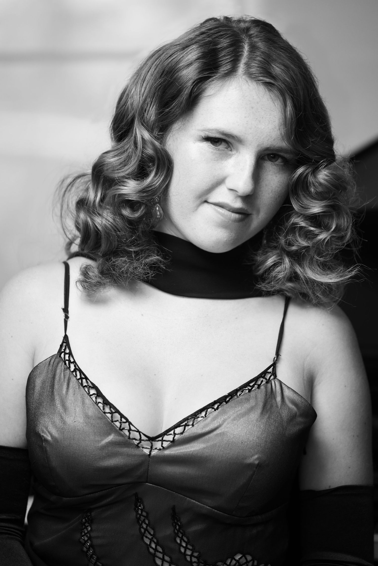Black and white portrait of a young woman with curly hair wearing a spaghetti strap dress and choker necklace.