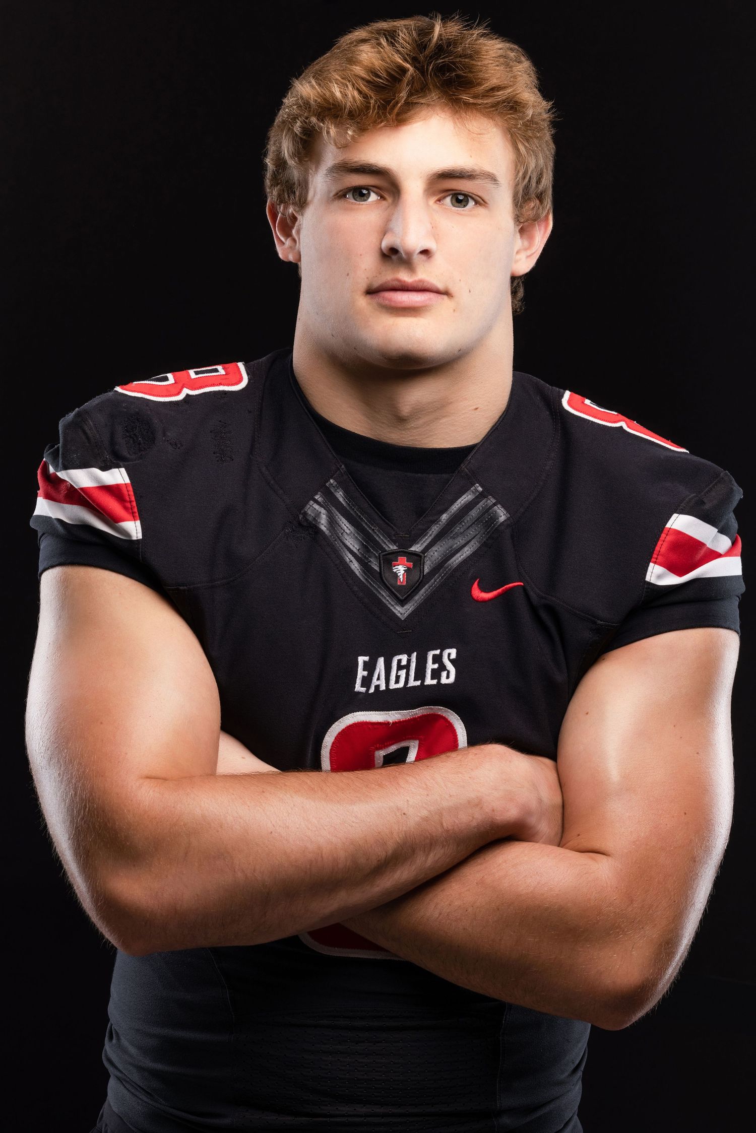 Muscular teen football player in Eagles black jersey posing with arms crossed on dark background.