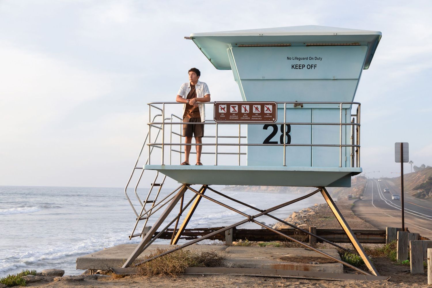 Man stands atop lifeguard tower 28 on a California beach at dusk.