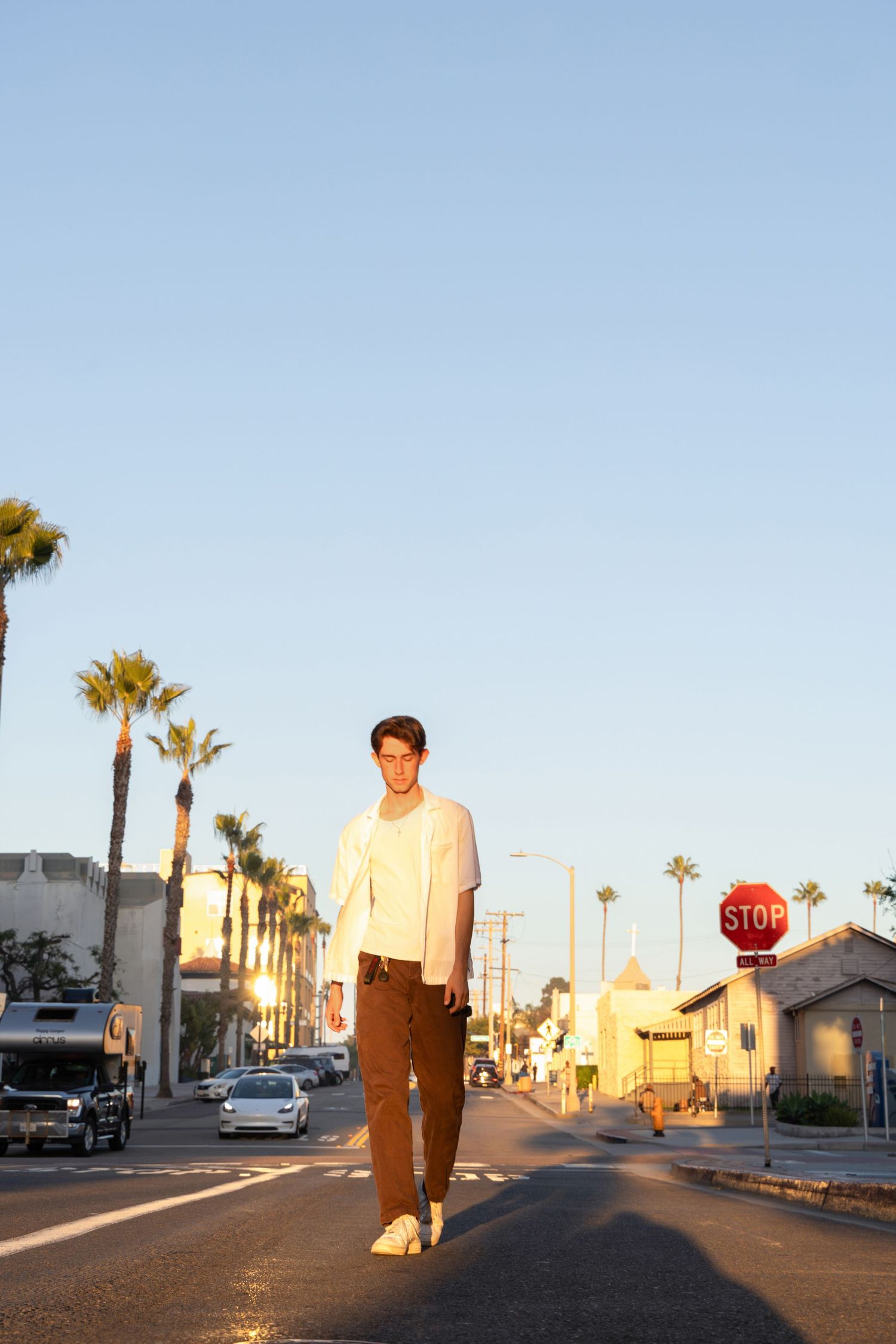 Young man standing in the middle of a sunny street lined with palm trees and a stop sign in a California neighborhood.