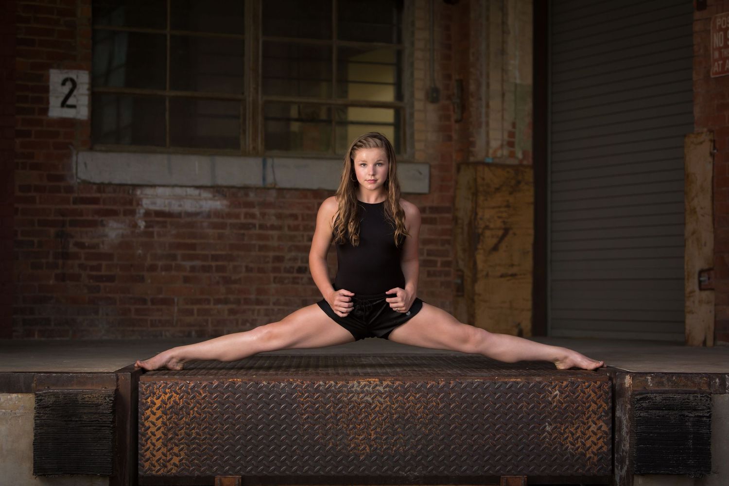 Female dancer performing a full split on a metal surface in front of a brick building.