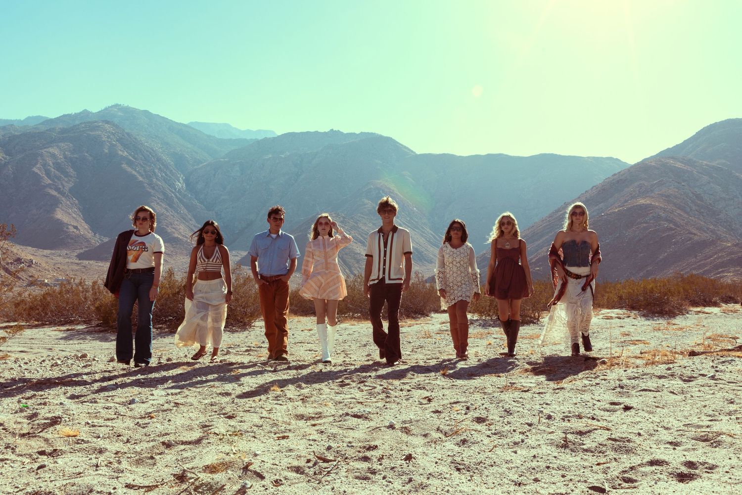 Group of eight people standing in a desert landscape with mountains in the background on a sunny day.