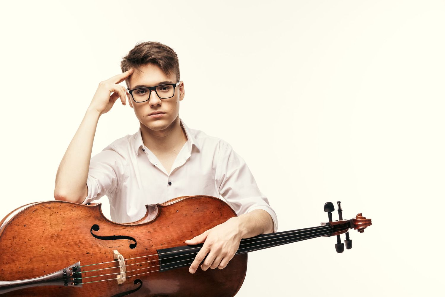 Portret wiolonczelisty z wiolonczelą w studio na jasnym tle, kadr w półzbliżeniu