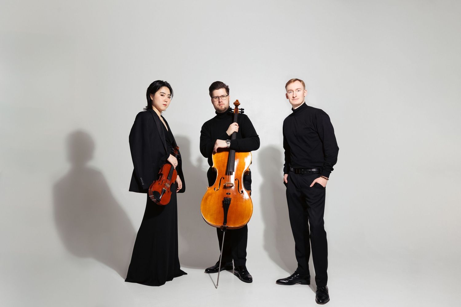 Trio z wiolonczelą na jasnym tle, minimalistyczna fotografia promocyjna