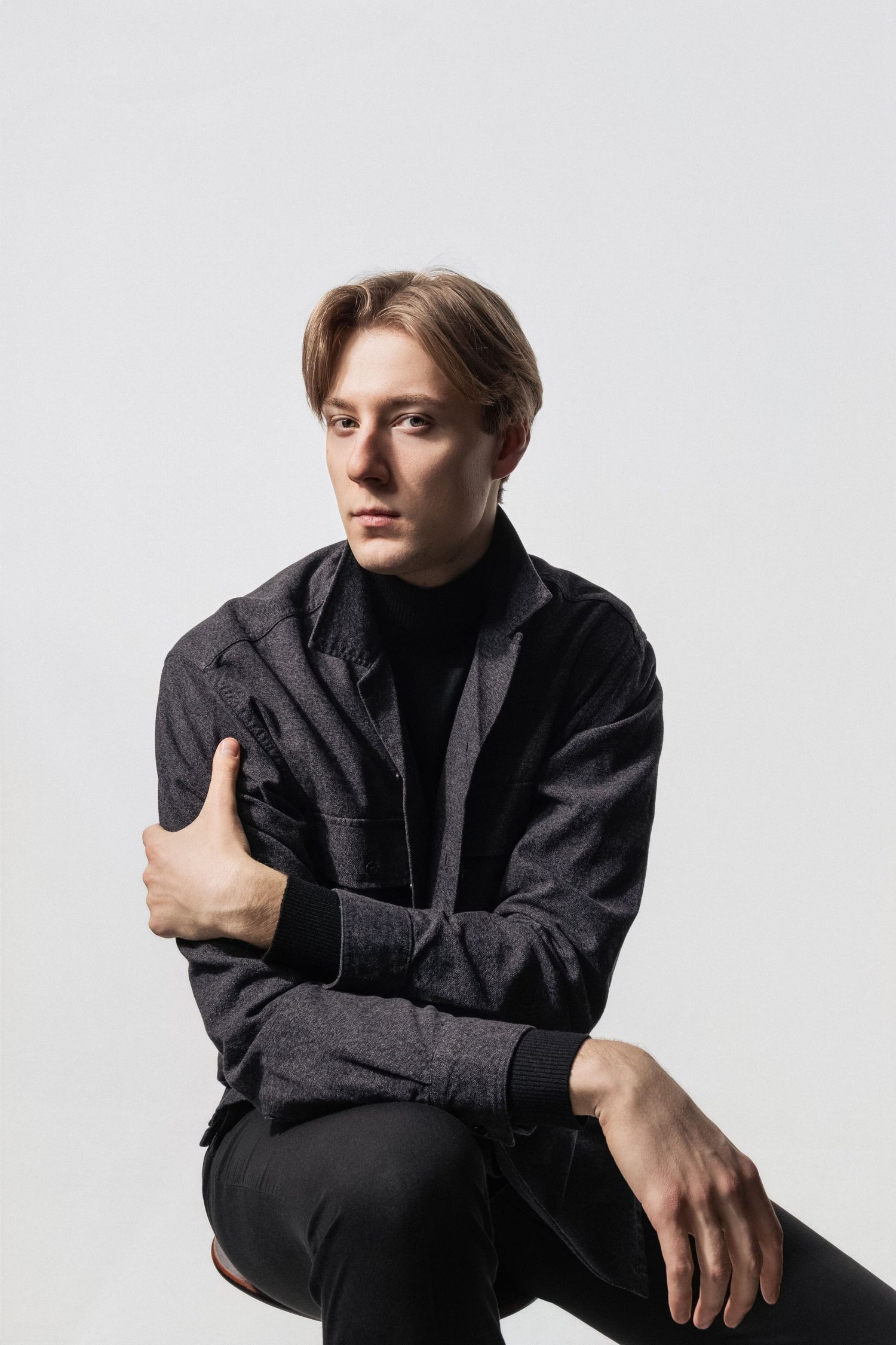 Mężczyzna siedzący w studio na jasnym tle, spokojny portret wizerunkowy