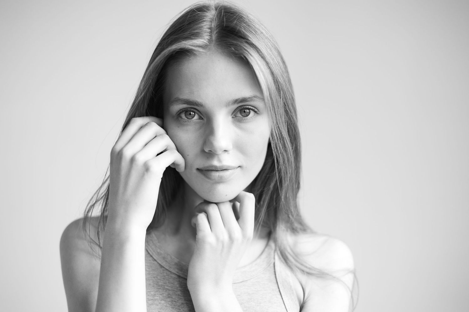 Czarno-biały portret kobiety z dłońmi przy twarzy, delikatna fotografia wizerunkowa