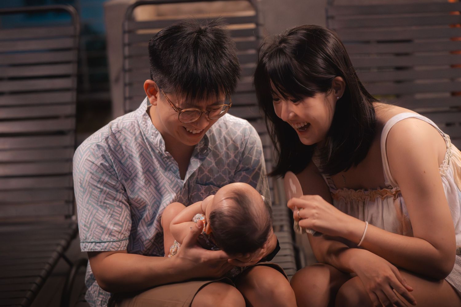 Parents share a joyful moment with their baby while sitting together on a wooden bench.