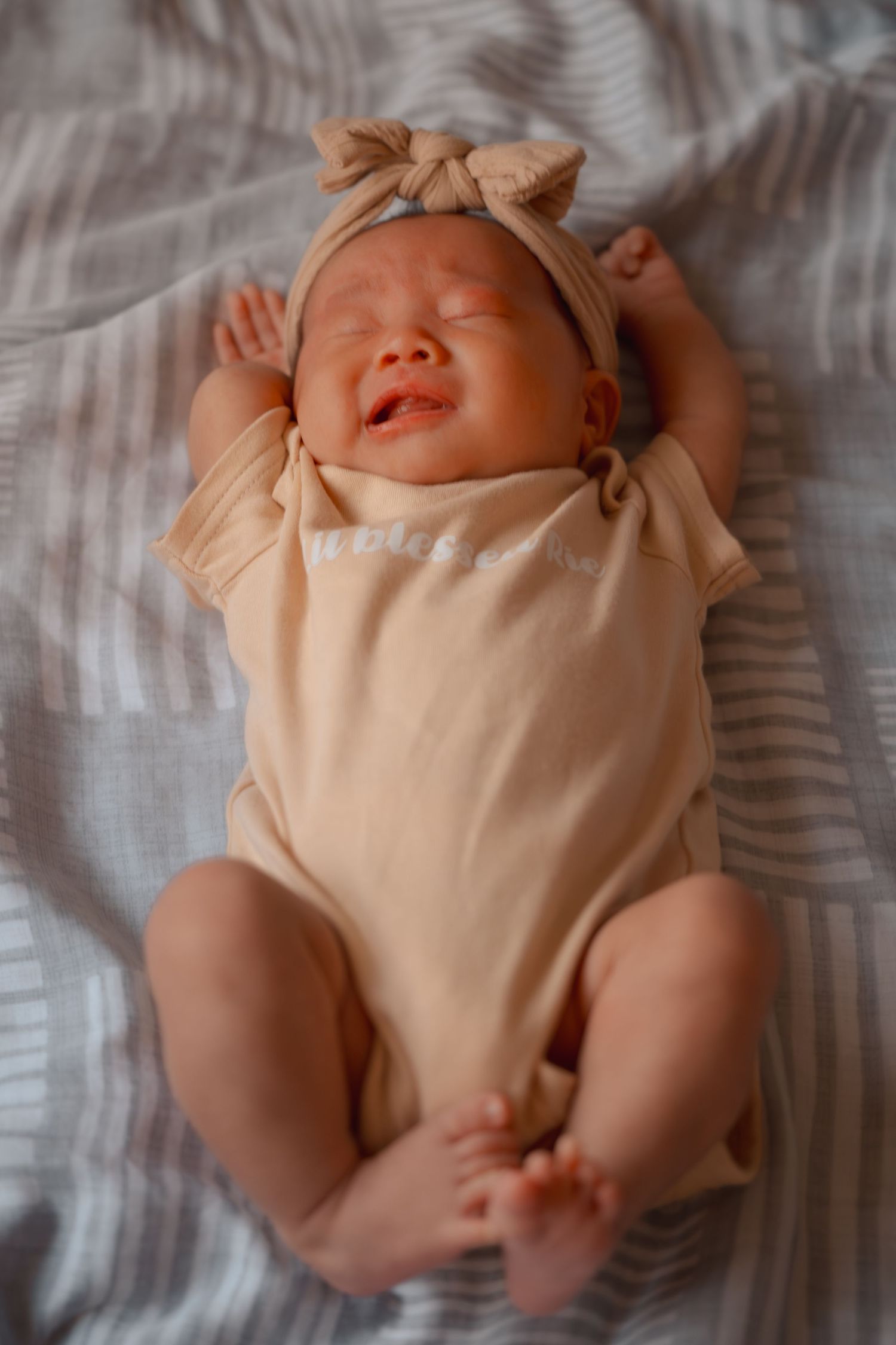 Newborn baby in cream outfit lying on white textured bedding.