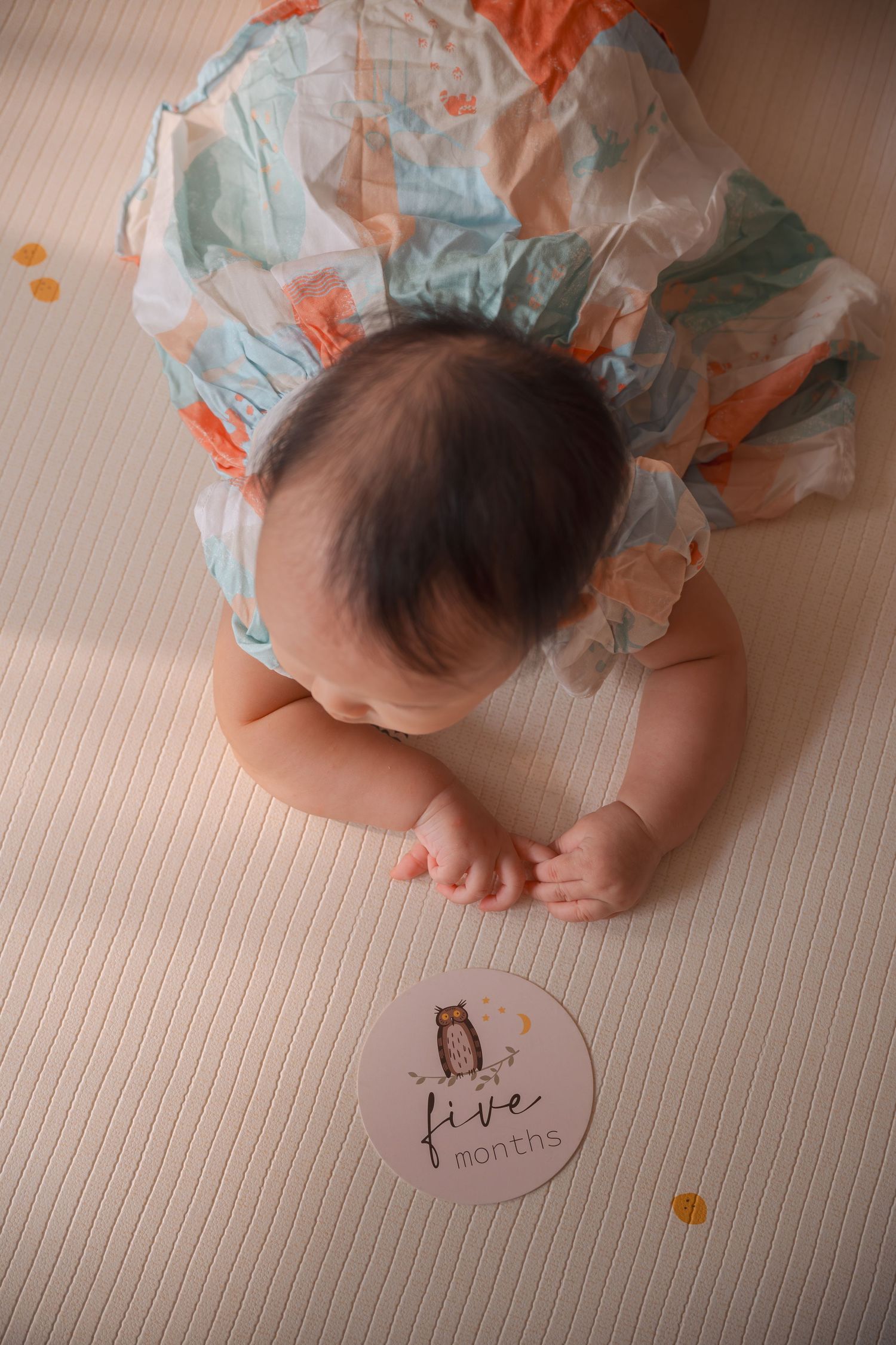 Baby wearing a diaper crawls across wooden floor with milestone markers showing monthly growth progress.