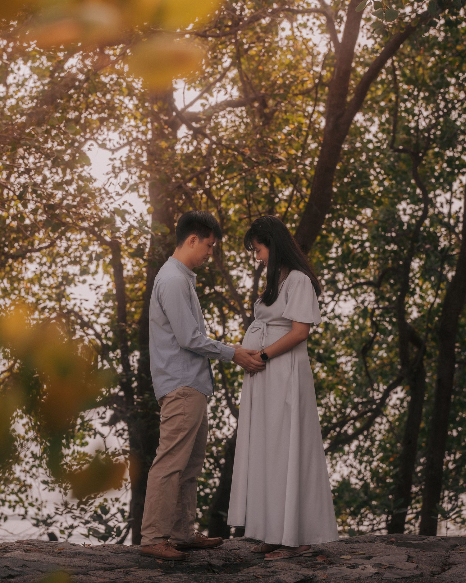 Couple standing together among autumn trees during sunset.