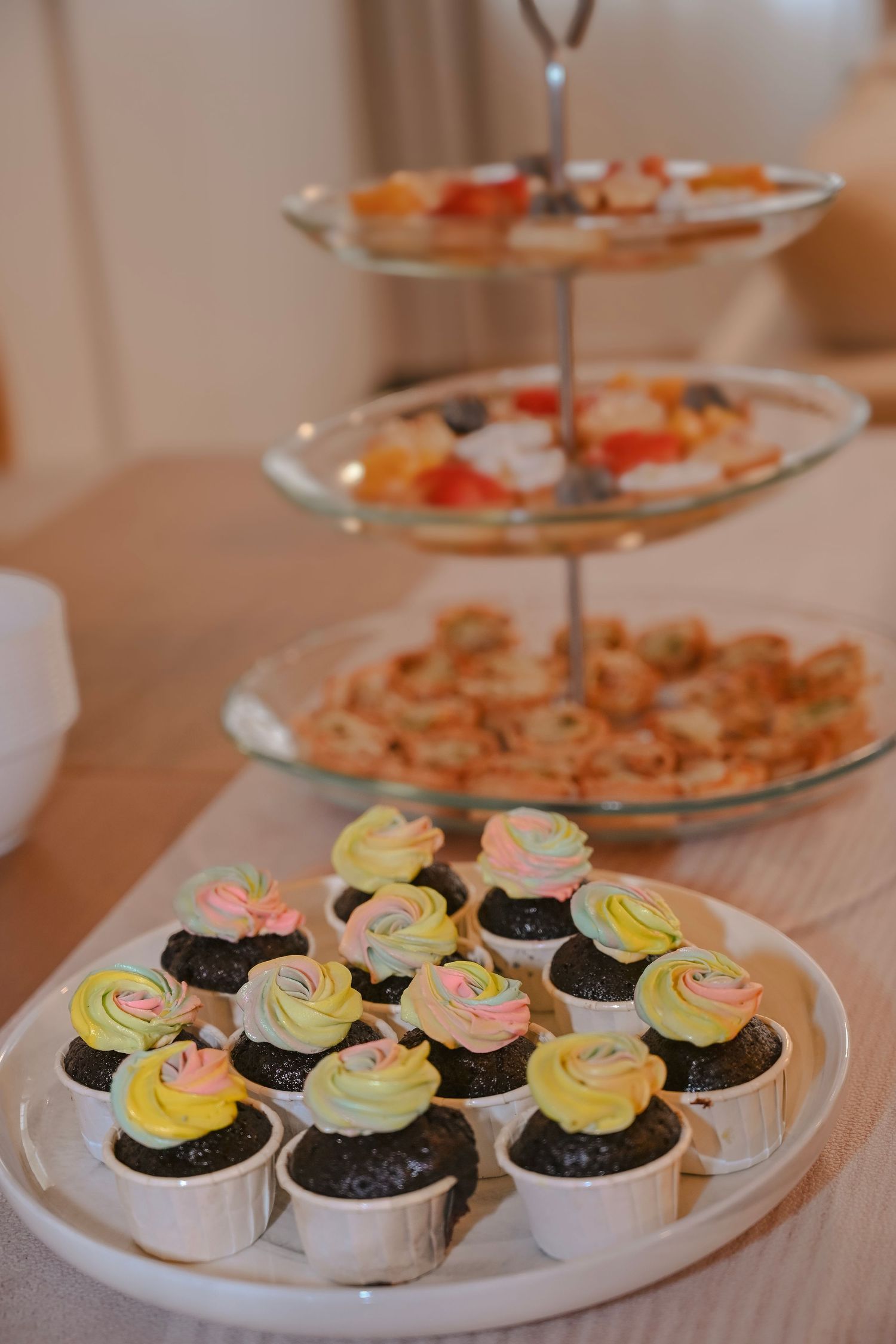 Tiered serving tray with decorated cupcakes in pink and yellow frosting at a party.