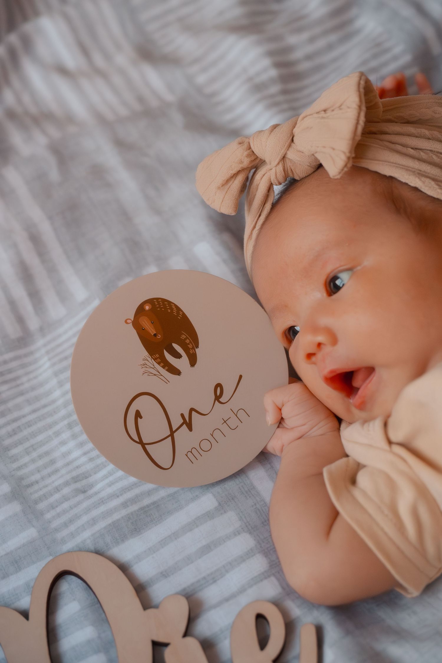 Close-up photo of a baby's face next to a wooden milestone marker on soft gray fabric.