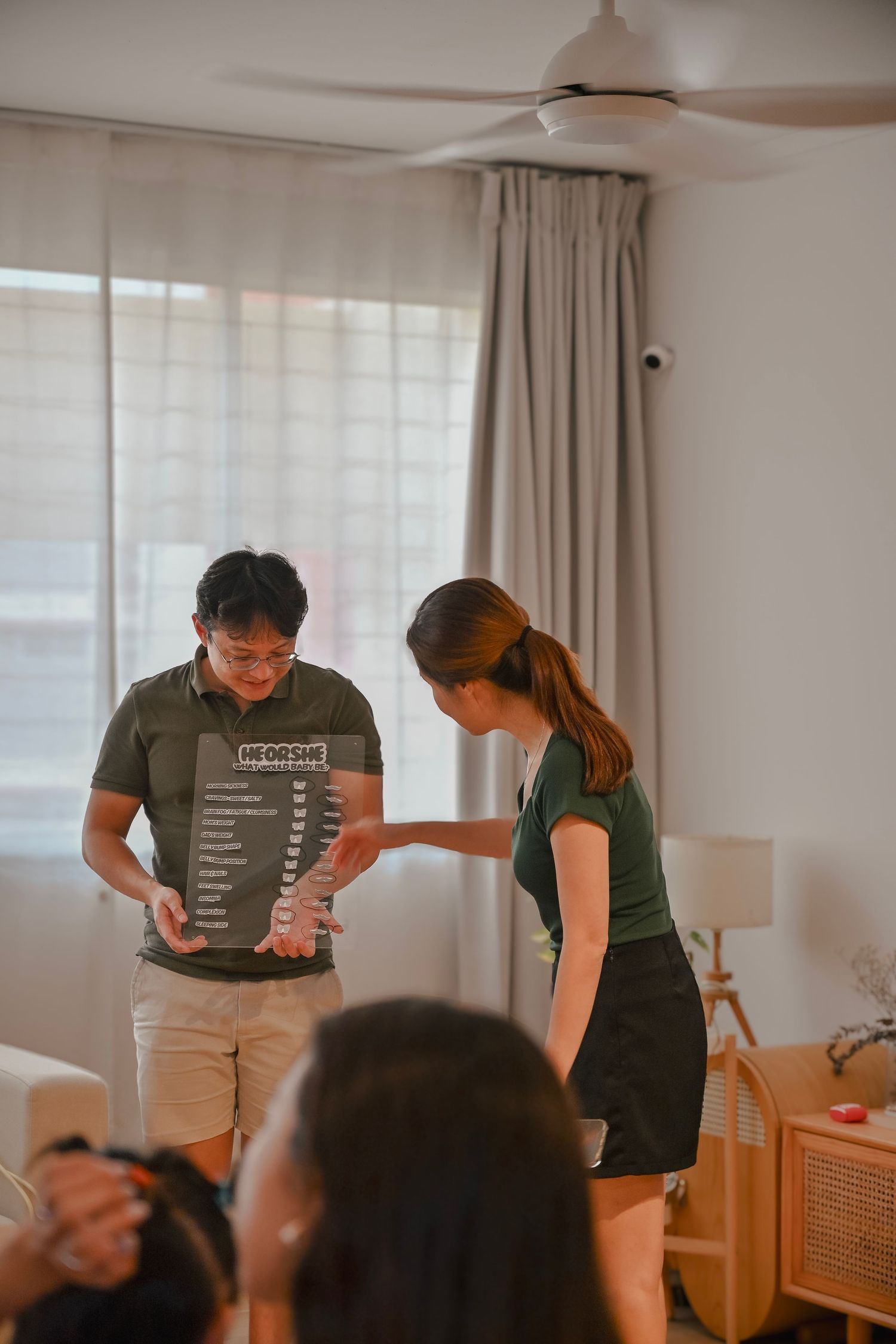 Man and woman reviewing a dark menu board together indoors near a bright window with ceiling fan.