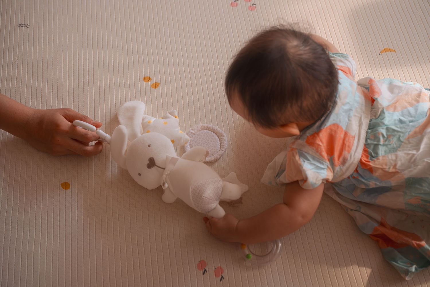 Baby playing with white stuffed animal toys on a padded floor mat with colorful confetti scattered around.