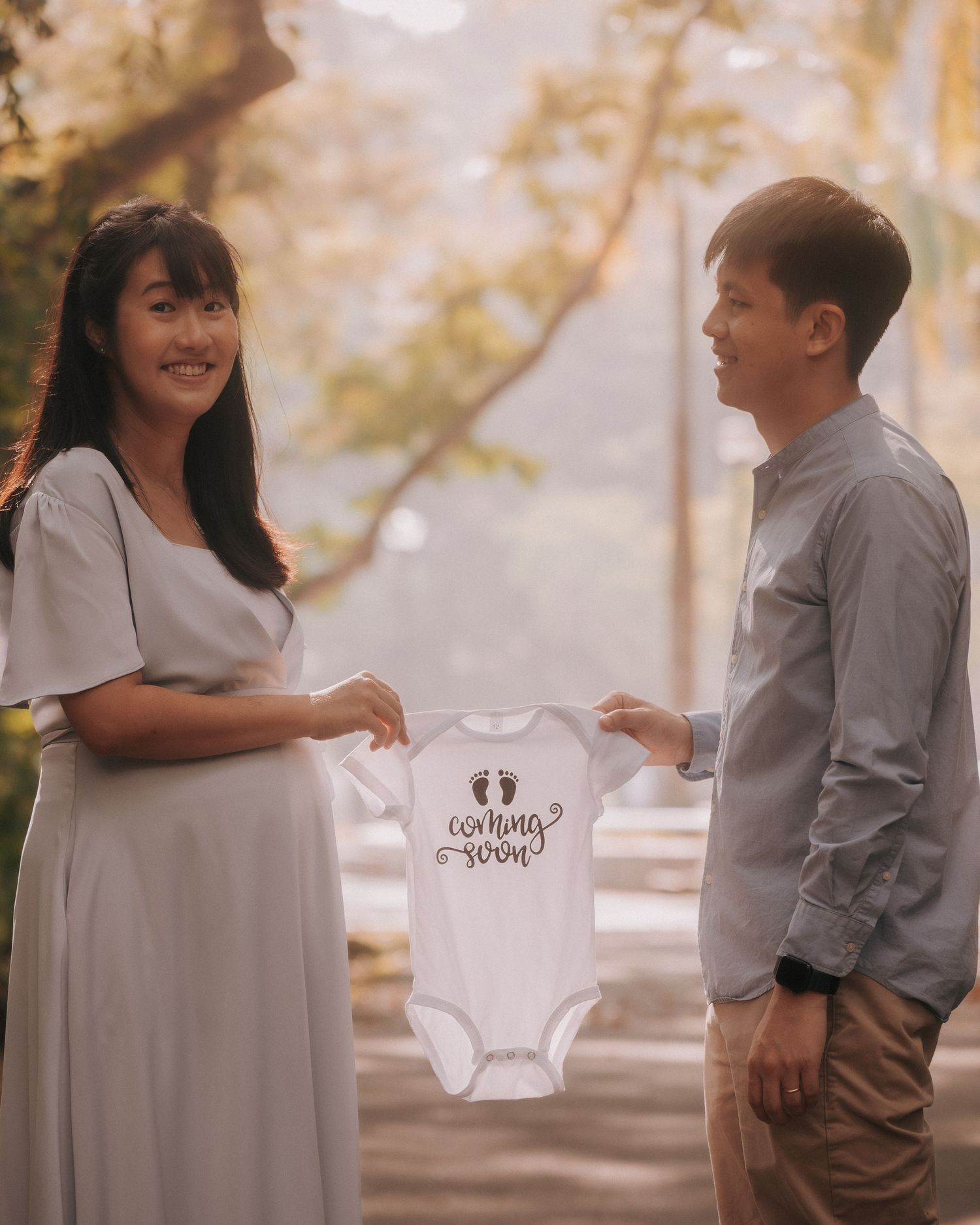 A couple shares a tender moment outdoors while holding a baby onesie.