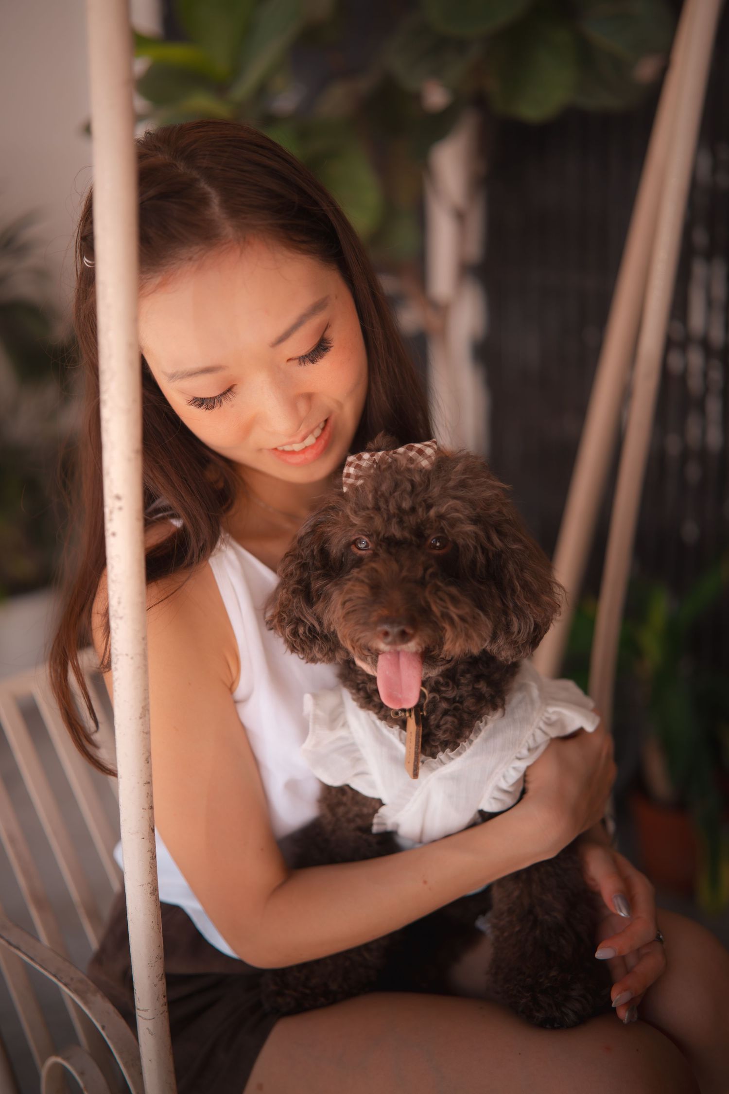 A woman in white holds and cuddles with a small brown curly-haired dog while sitting on a porch swing.