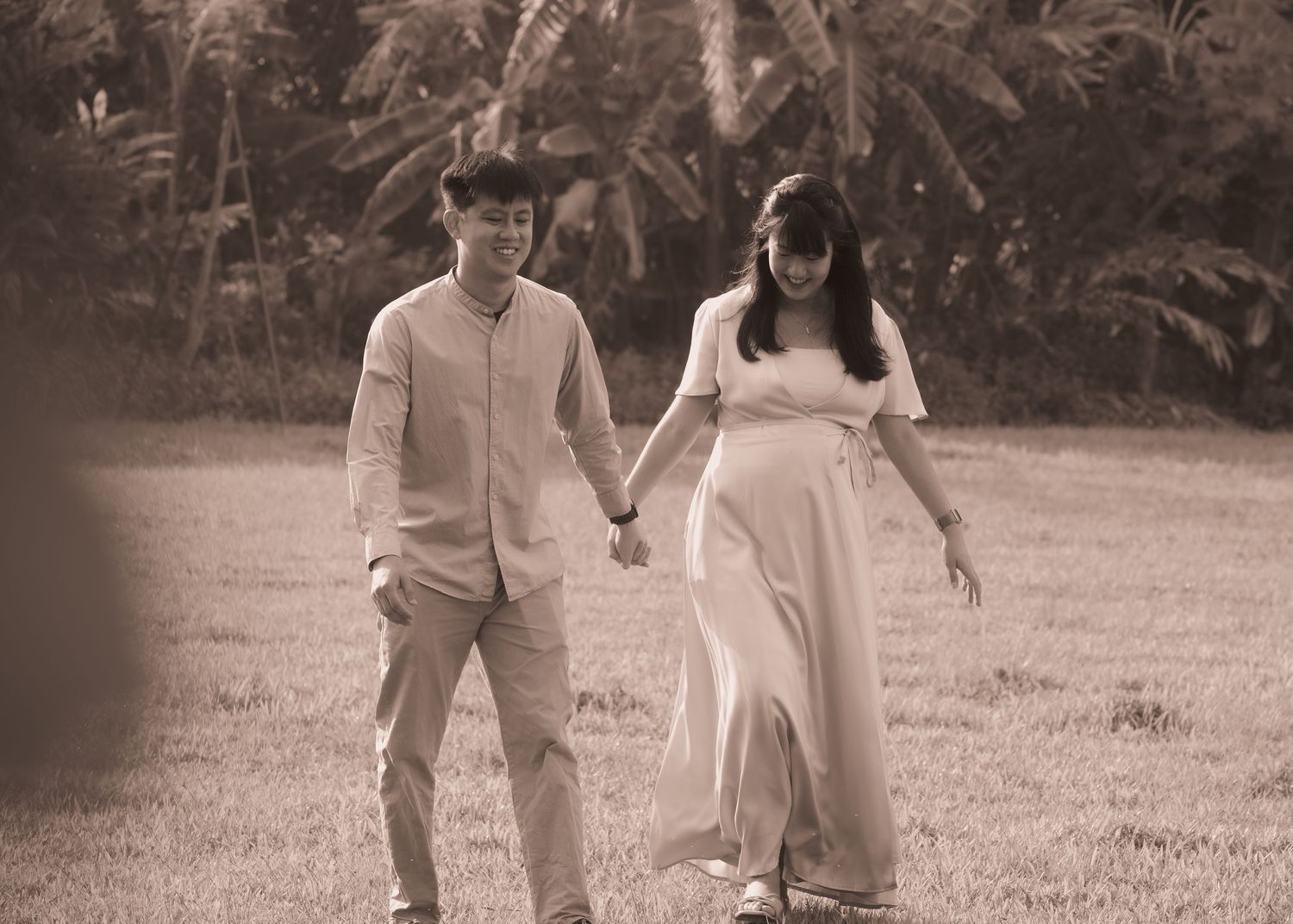 A couple in light colored outfits walks together through a scenic outdoor setting during golden hour.