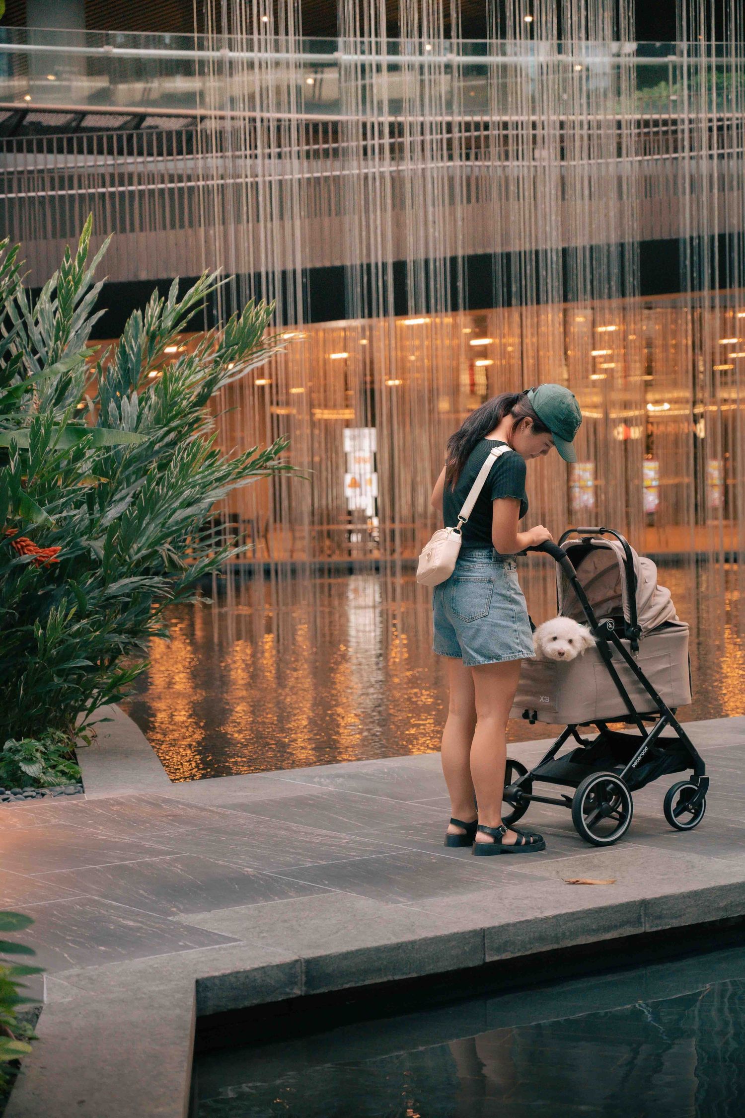 Person with stroller walking along a modern building with hanging string lights.
