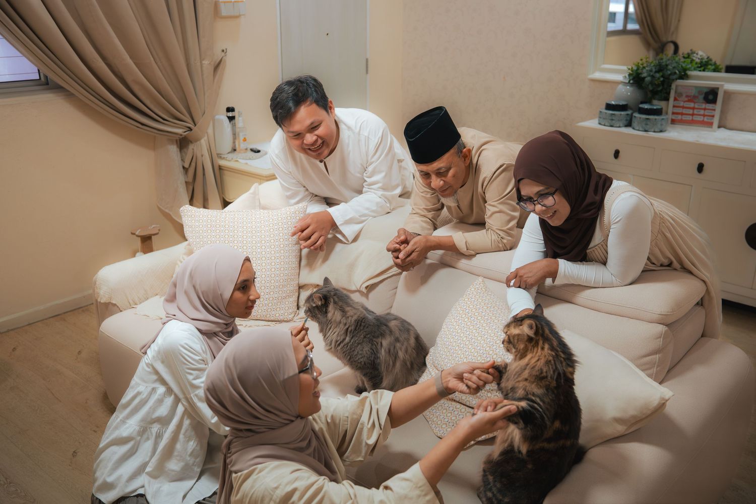 Muslim family gathered on sofa petting cats together in a cozy living room during Eid celebration.