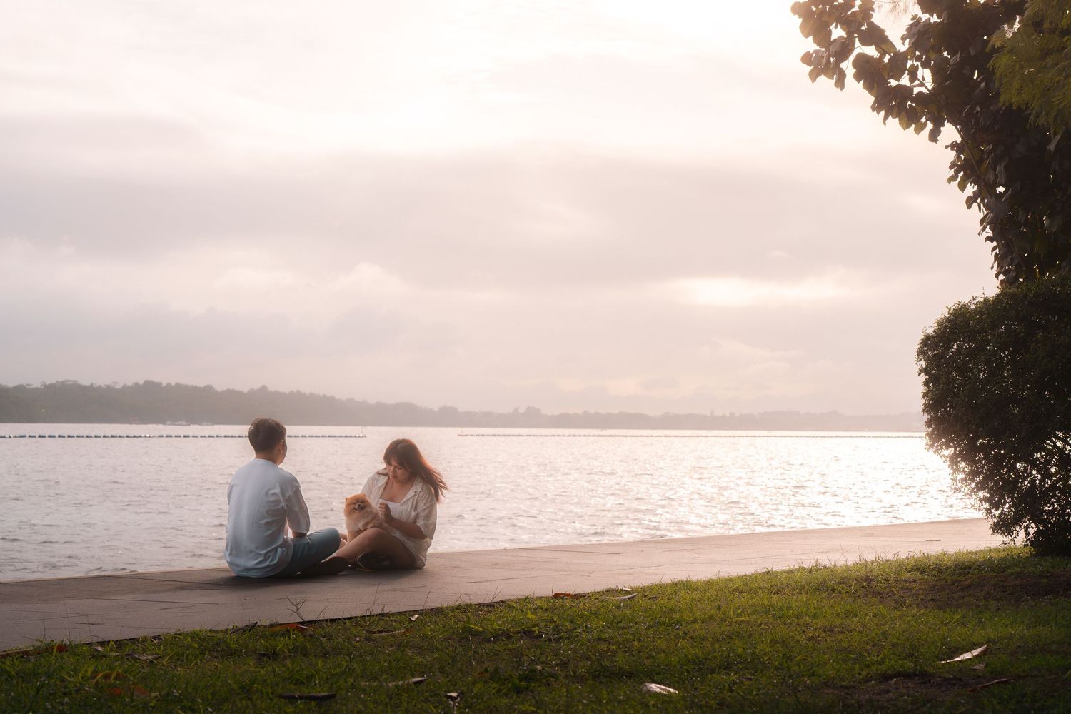 Couple sitting on a wooden dock by a calm lake at sunset, enjoying a peaceful moment together in nature.