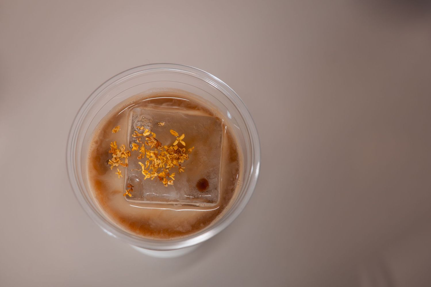 A glass of whiskey cocktail garnished with gold flakes and a large ice cube rests on a wooden surface.