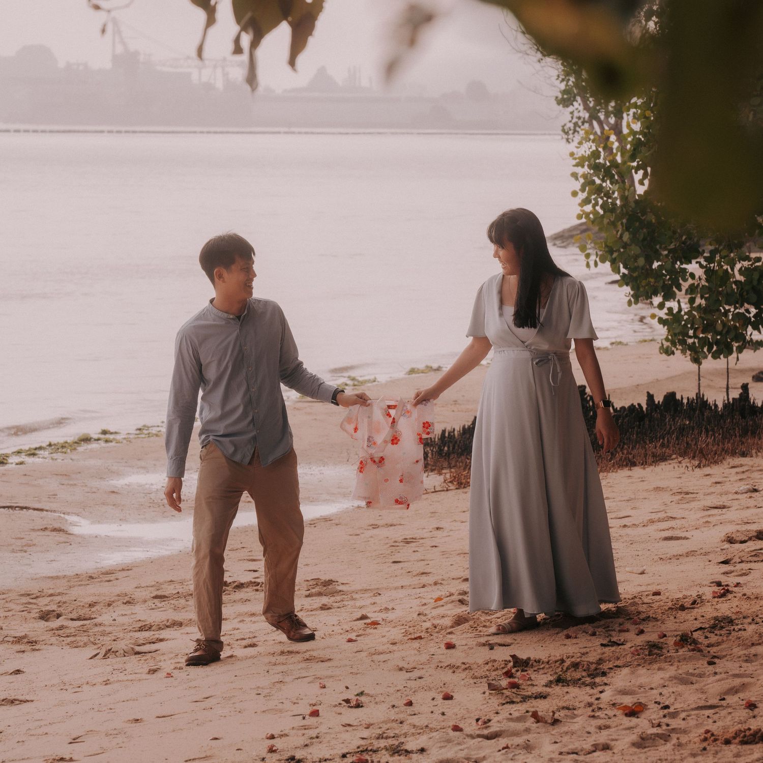 A couple walks along a sandy beach during sunset in matching gray and white outfits.