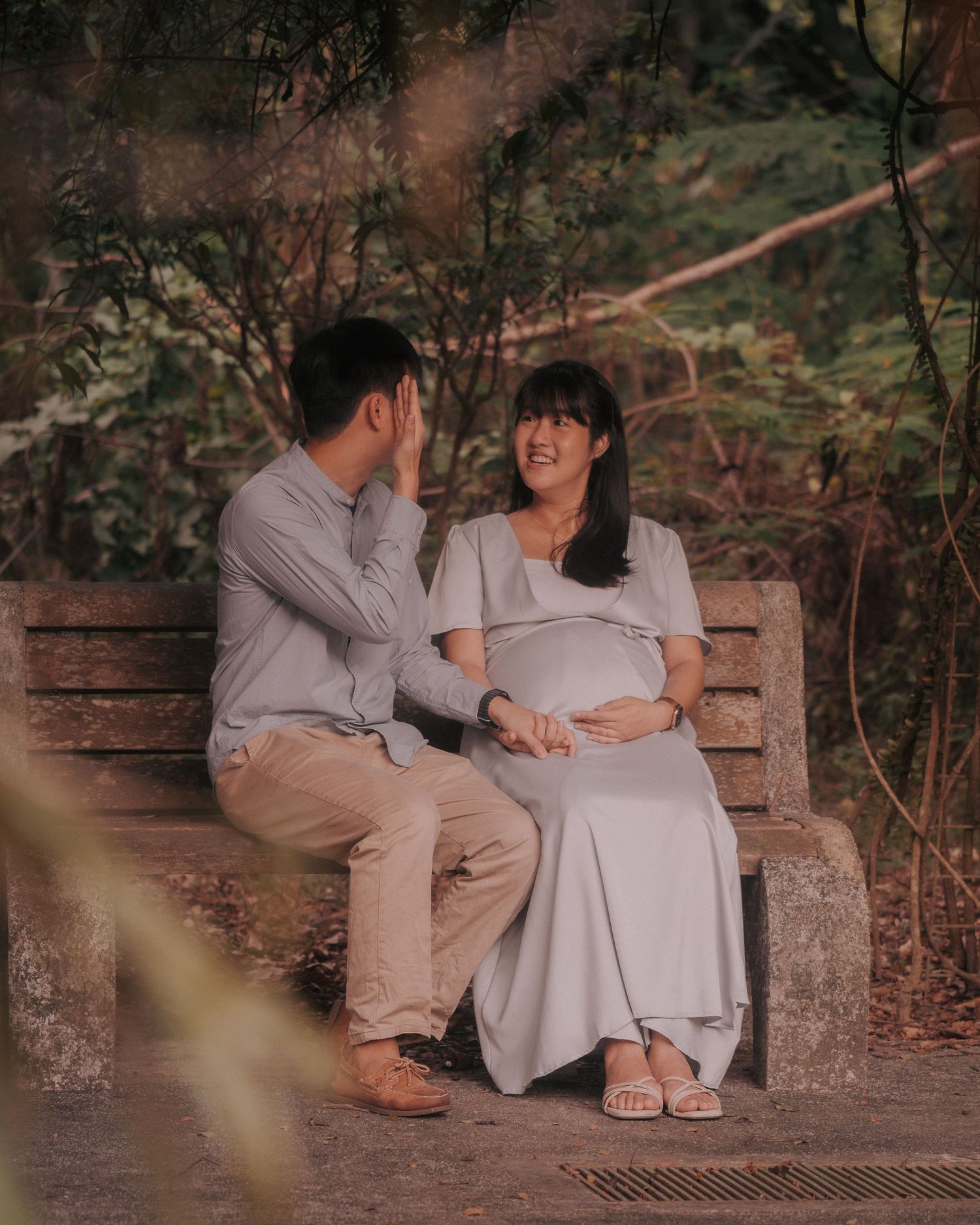 A couple sits close together on a rustic stone bench surrounded by greenery.
