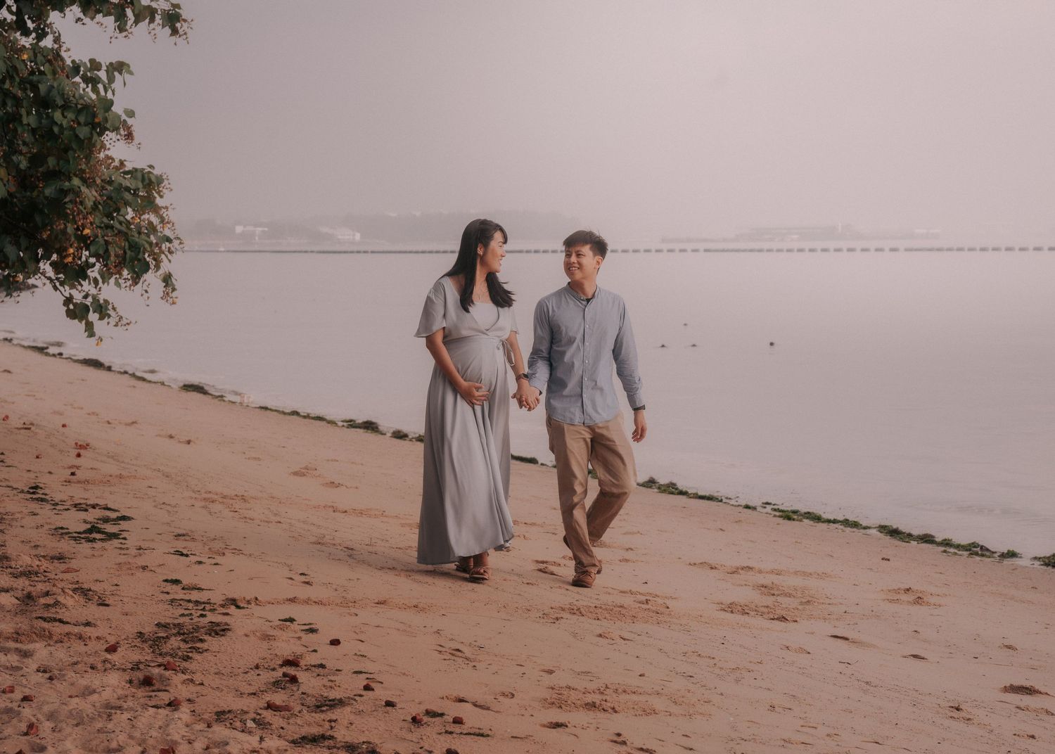 A couple walks together along a sandy beach shore during sunset while holding hands.