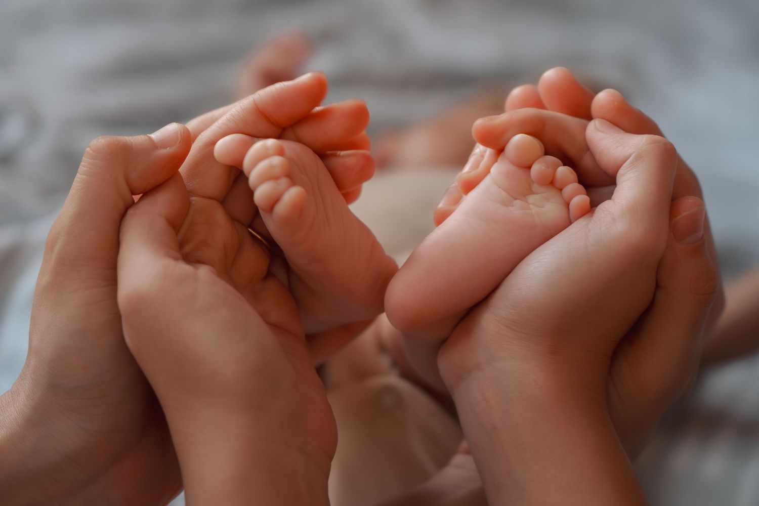 Two adult hands gently cradling tiny newborn baby feet, symbolizing parental love and new life.