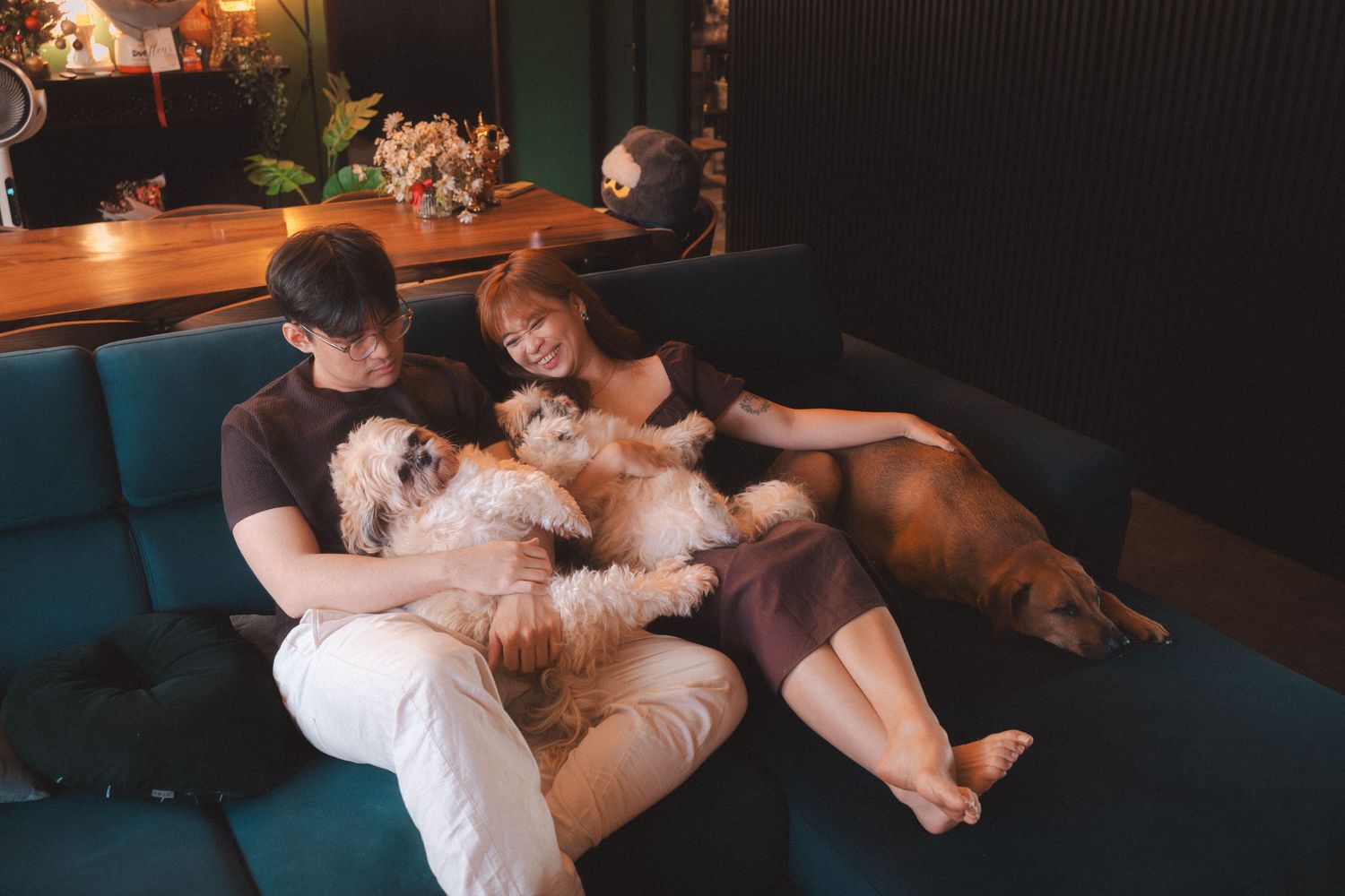 Two people lying down and cuddling with a brown dog on a couch.