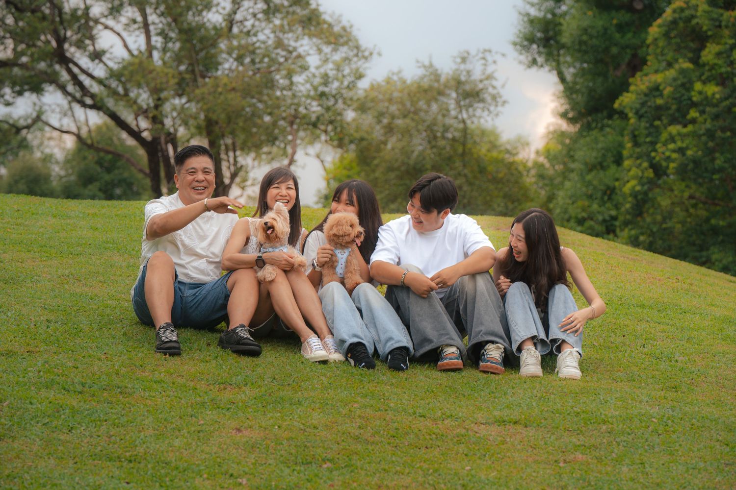 Asian family sitting on green grass in a park, laughing and bonding together on a sunny day.