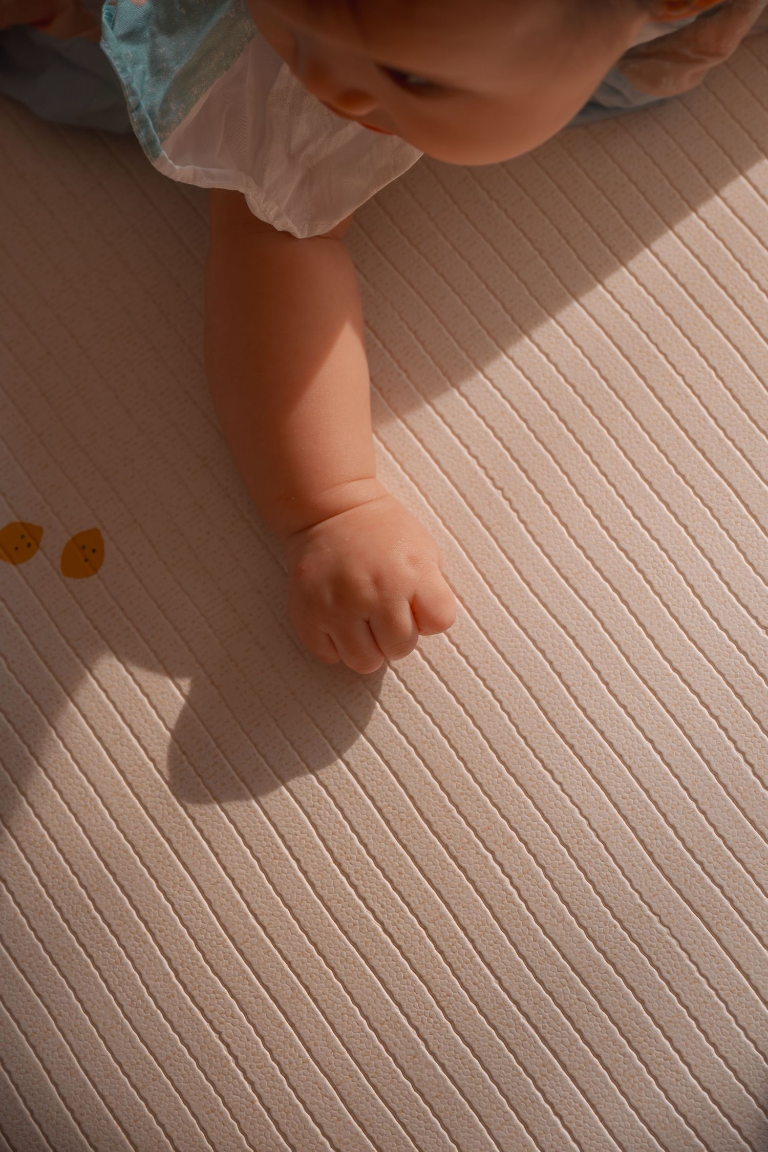 Close-up of a baby crawling on a light pink ribbed play mat, with tiny hand touching the surface.